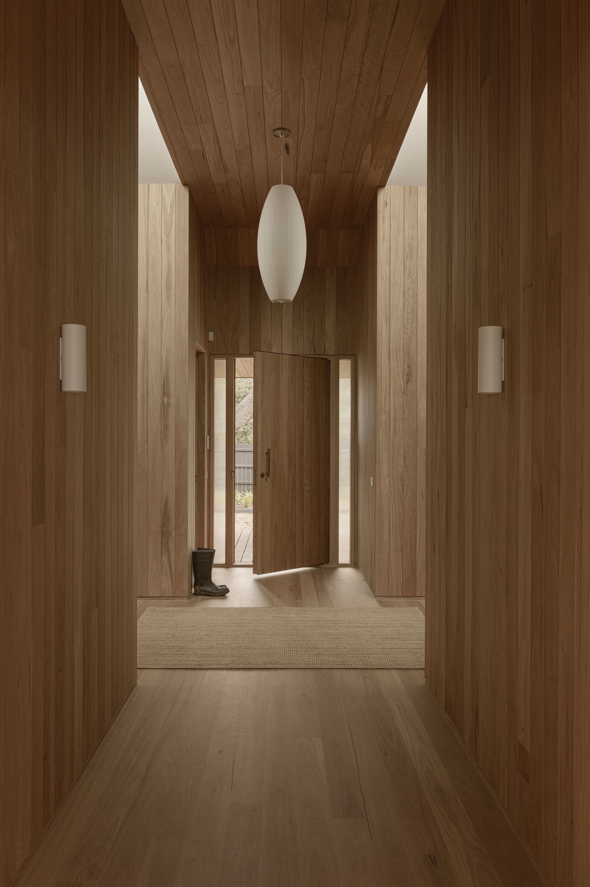 Timber-clad hallway with vaulted ceiling and white pendant light leading to an open entrance