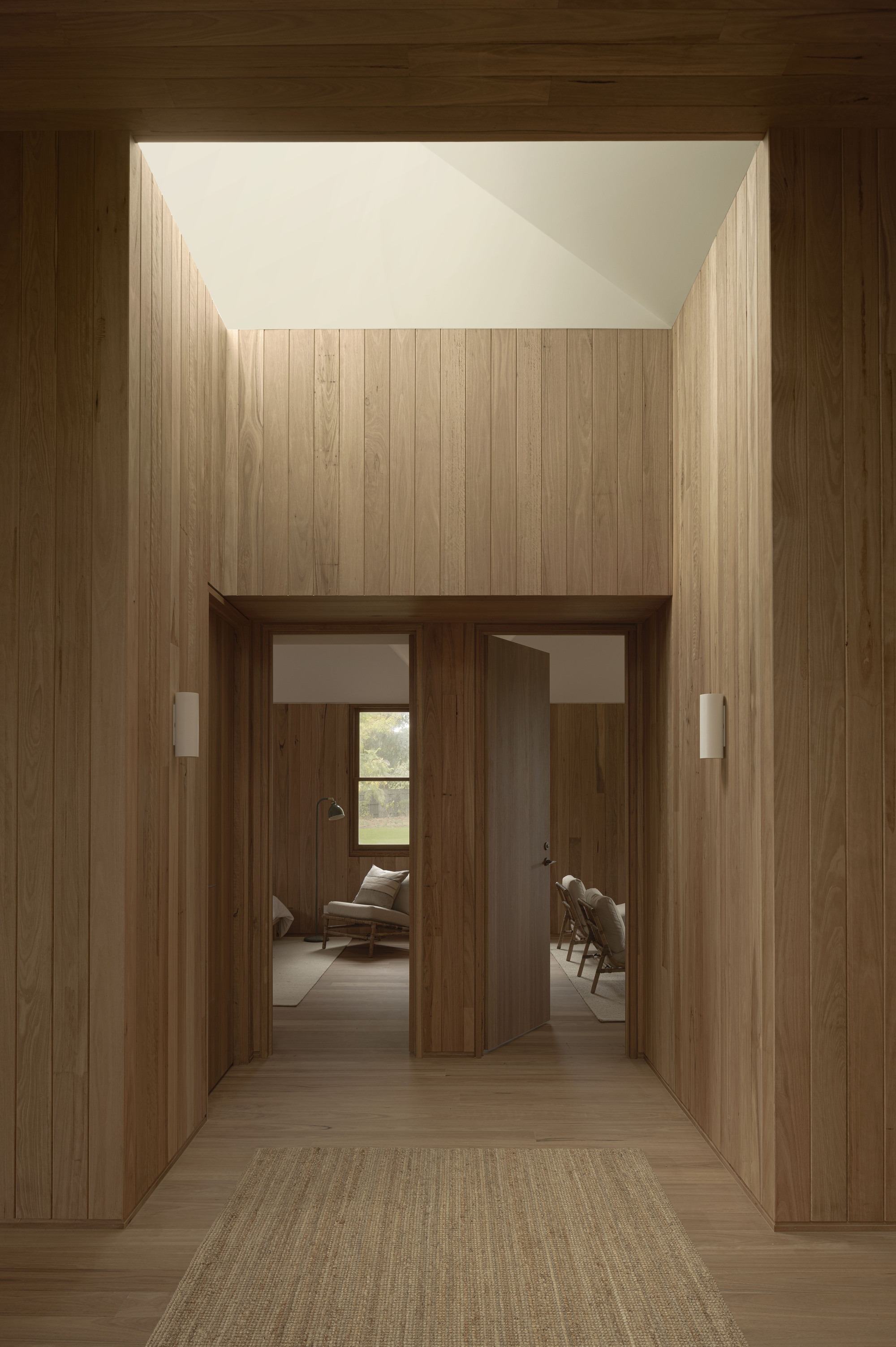 Entry hall framed by timber walls beneath a recessed skylight with paired doorways beyond