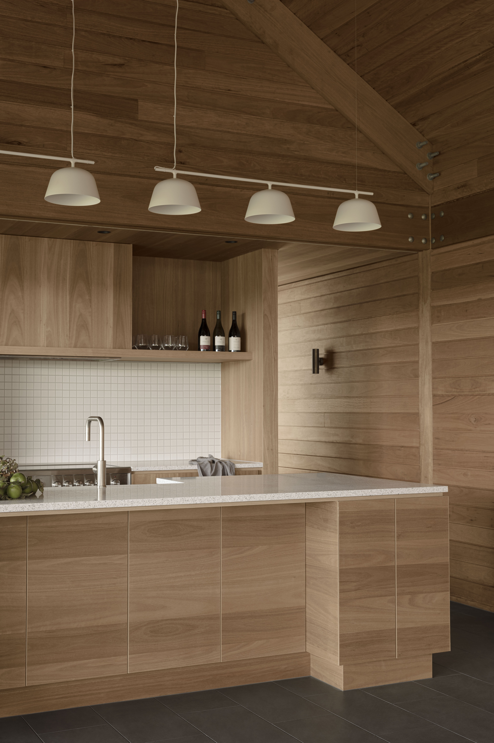 Kitchen island with white tile backsplash and timber cabinetry under a vaulted plank ceiling