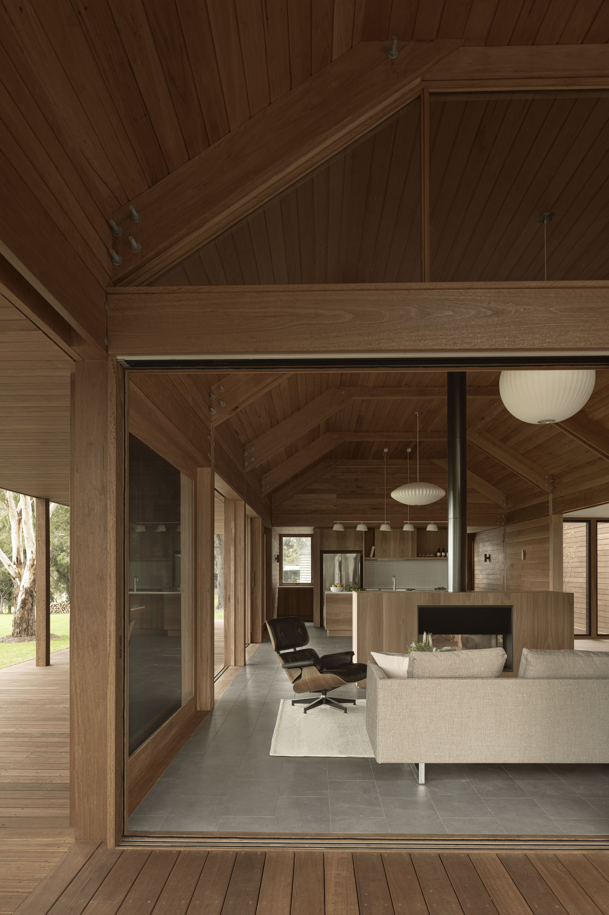 Open-plan living area with exposed timber beams and glazed doors connecting to the exterior deck