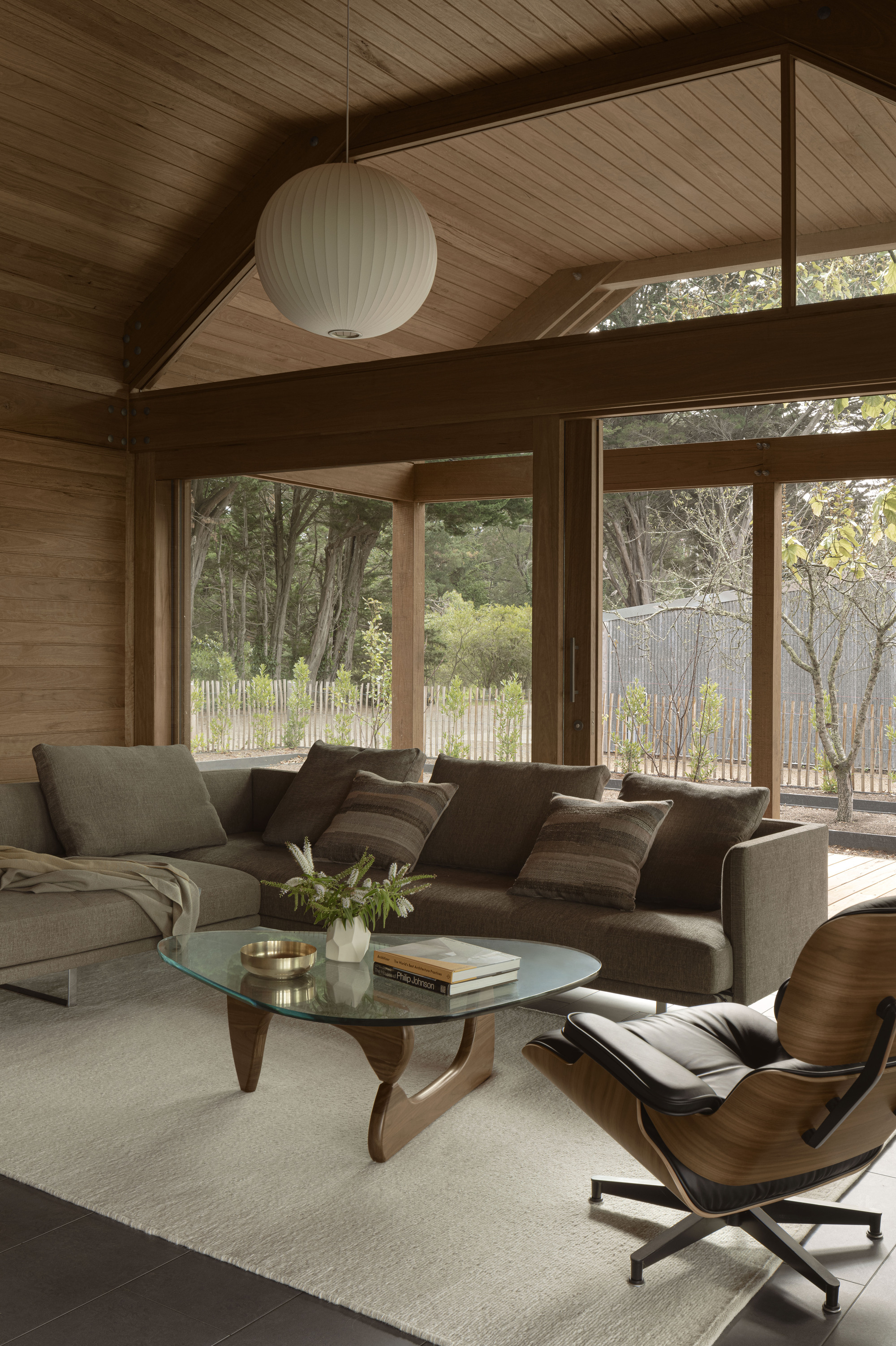 Living room with vaulted timber ceiling, clerestory windows, and views to surrounding trees through large glazing