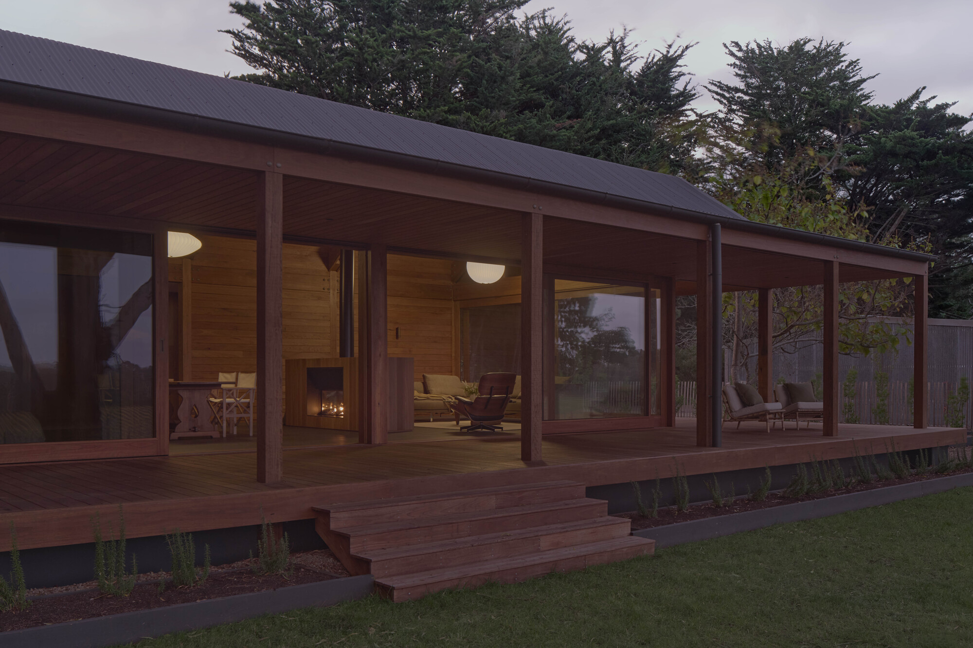 Glazed timber veranda with exposed posts and corrugated metal roof overlooking lawn at twilight