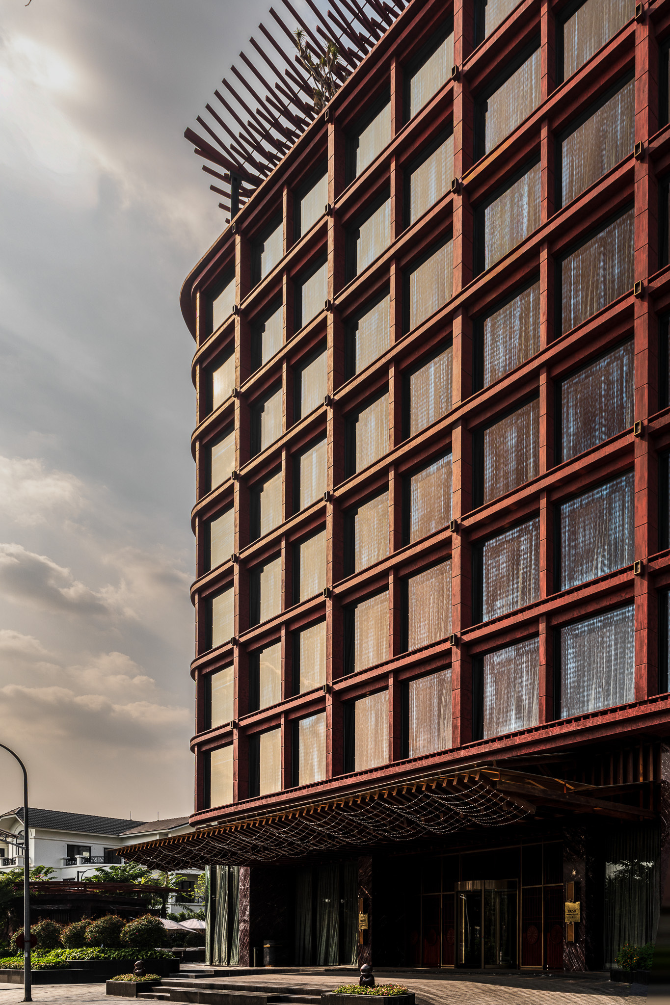 Red metal grid facade wrapping the curved corner above a canopied entrance under cloudy skies