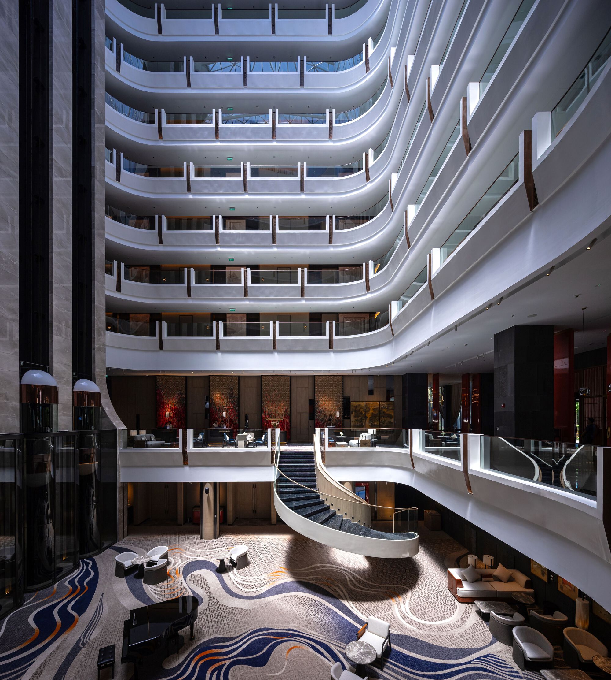 Multi-story atrium lobby with curved white balconies rising above a wavy patterned floor and twin staircases