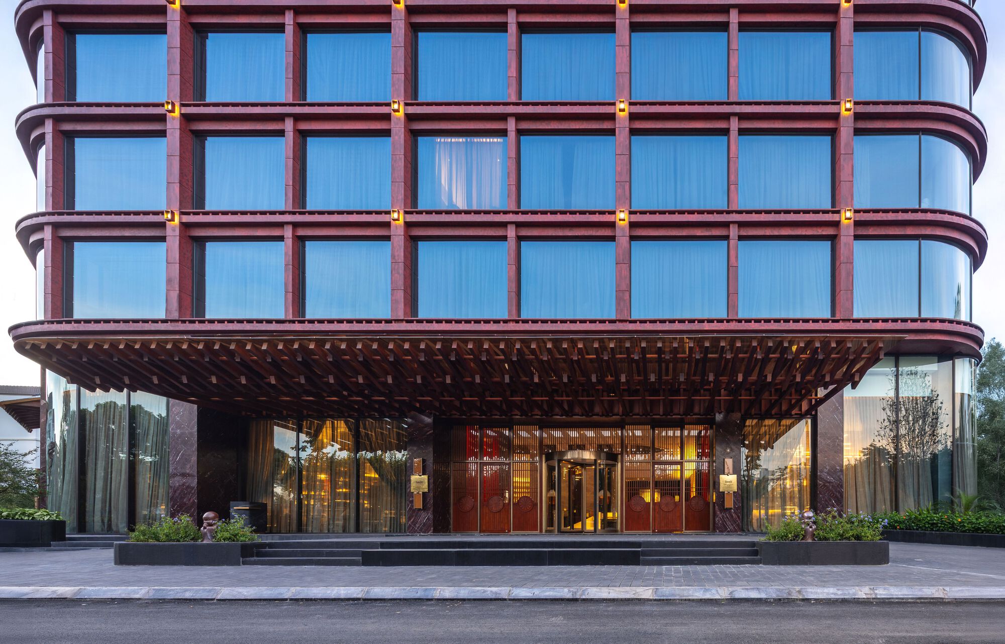 Entry canopy with rounded facade of bronze-framed windows above a covered porte-cochère at dusk