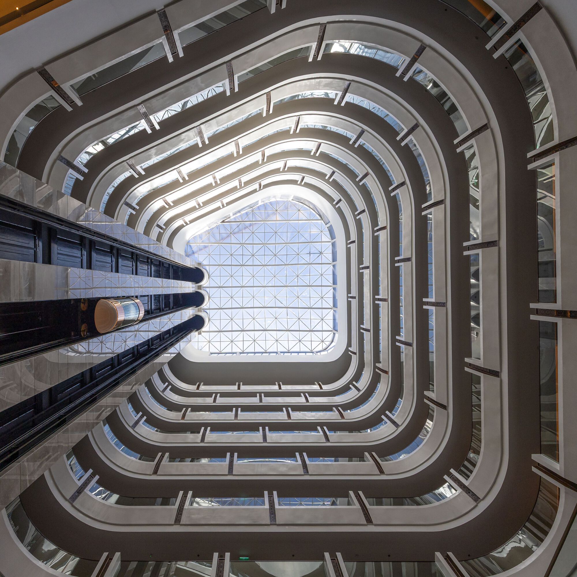 View up through the rounded atrium shaft with stacked balconies framing a glazed ceiling