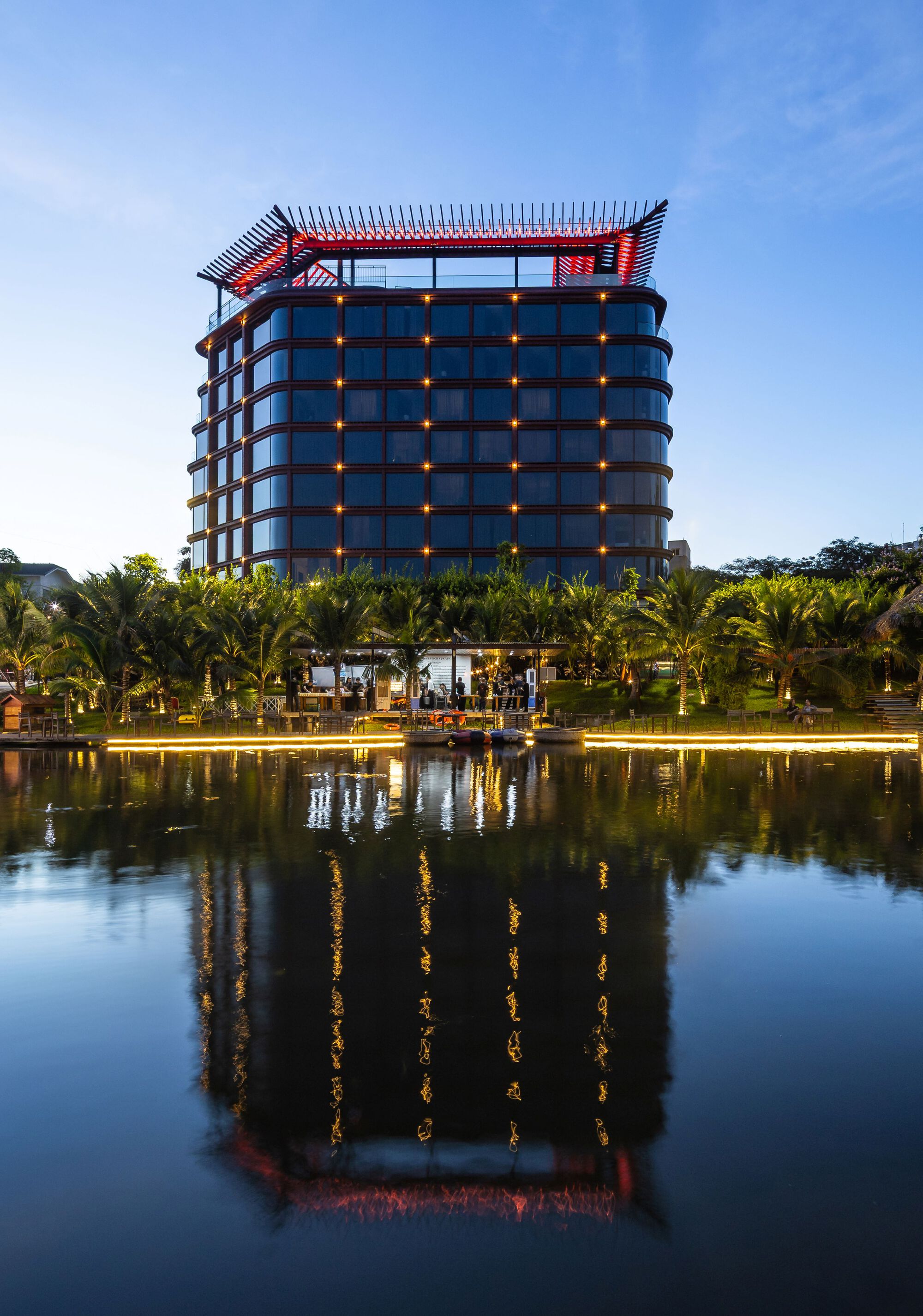 Curved tower with illuminated windows reflected in a landscaped pond at twilight