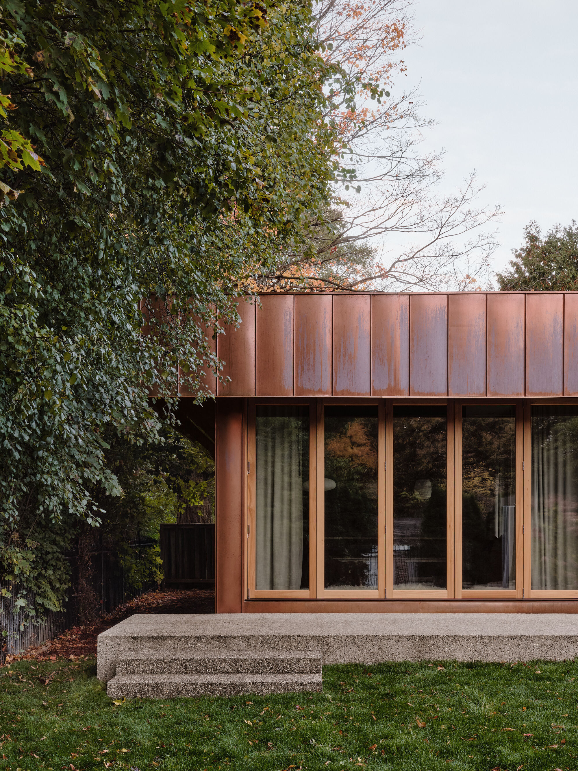 Corner detail of copper-clad volume with folding glass doors and adjacent ivy-covered wall