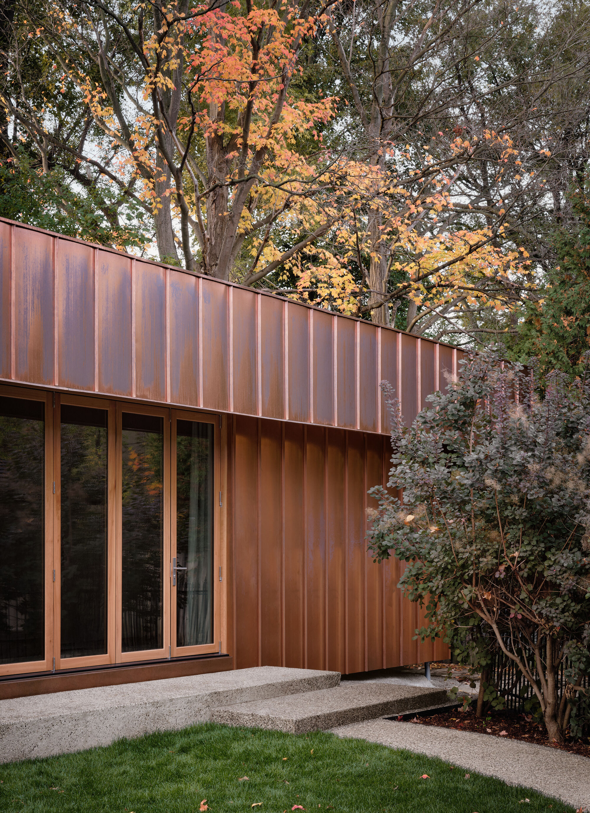 Copper facade with vertical joint detailing beneath trees showing autumn foliage