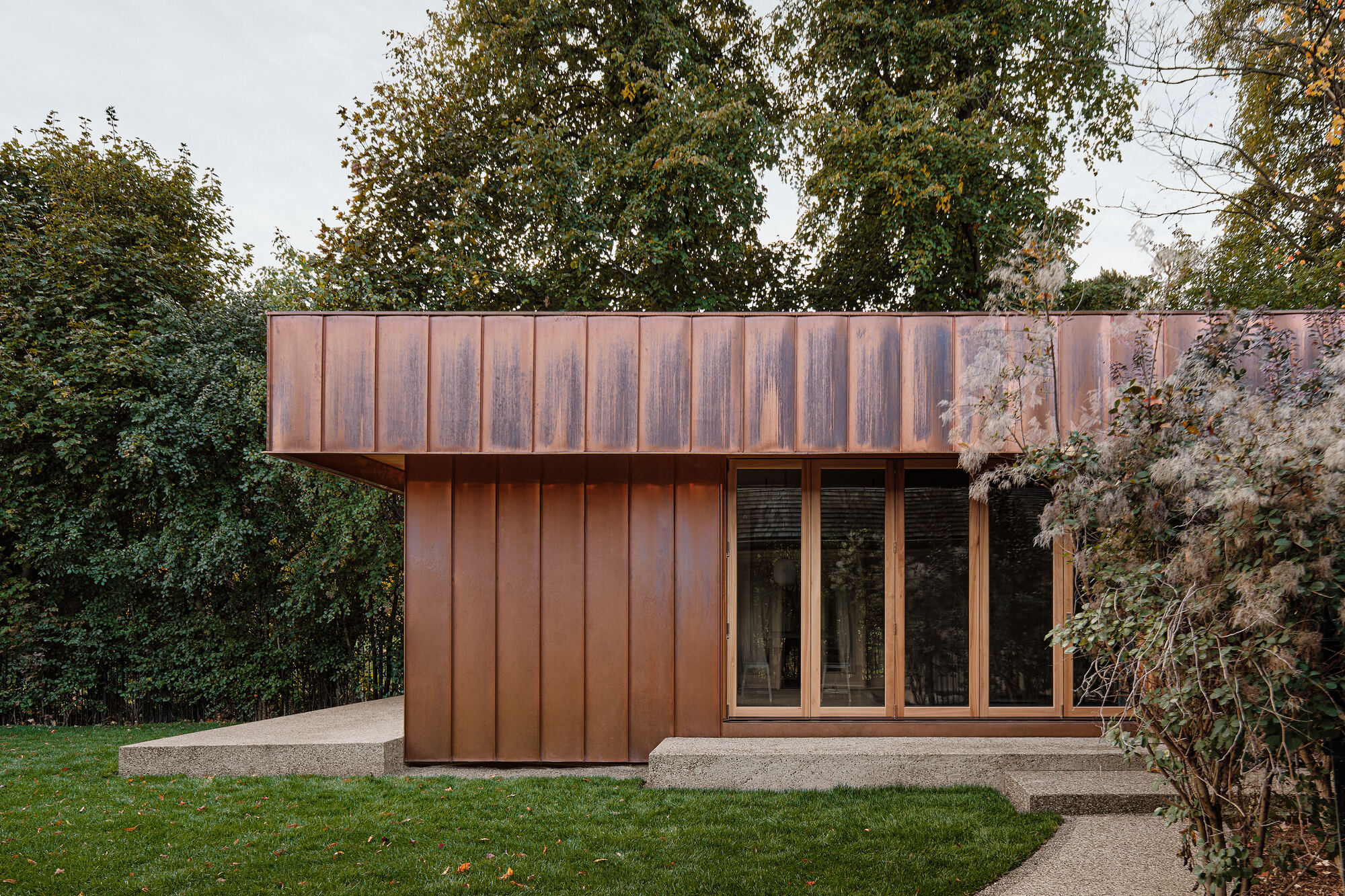 Garden pavilion with weathered copper cladding and glazed doors surrounded by lawn and mature trees