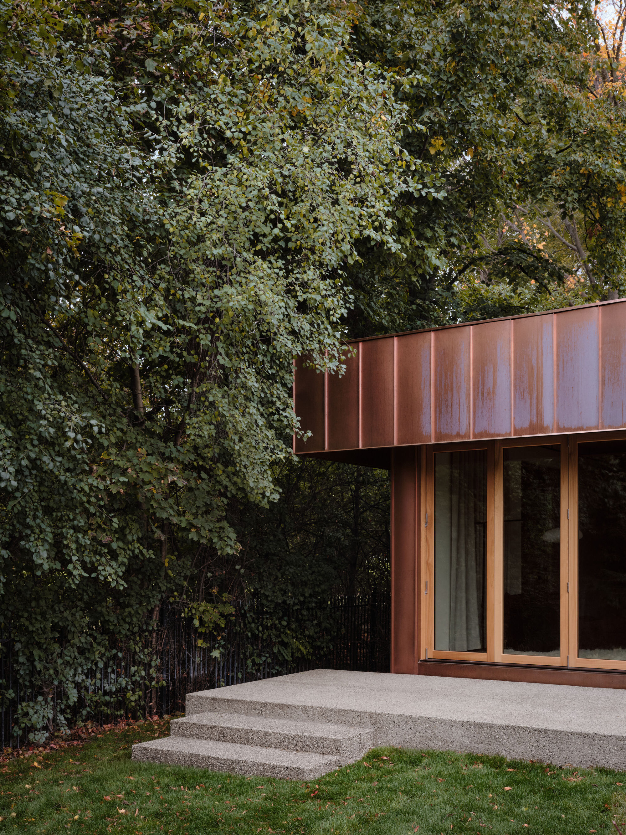 Cantilevered copper roof above glazed facade with exposed aggregate concrete terrace and steps
