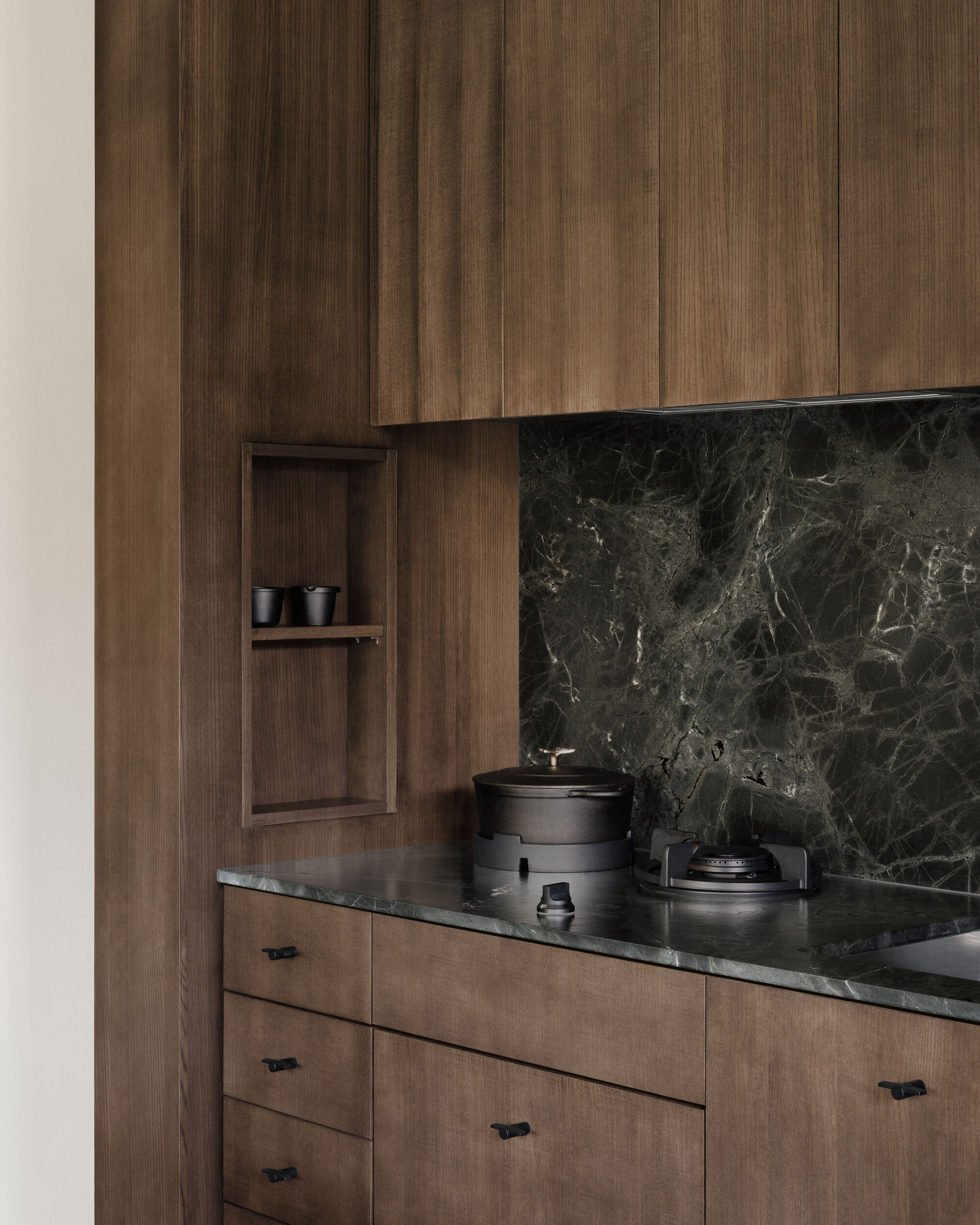 Close-up of timber cabinetry with dark veined stone backsplash and recessed display niche