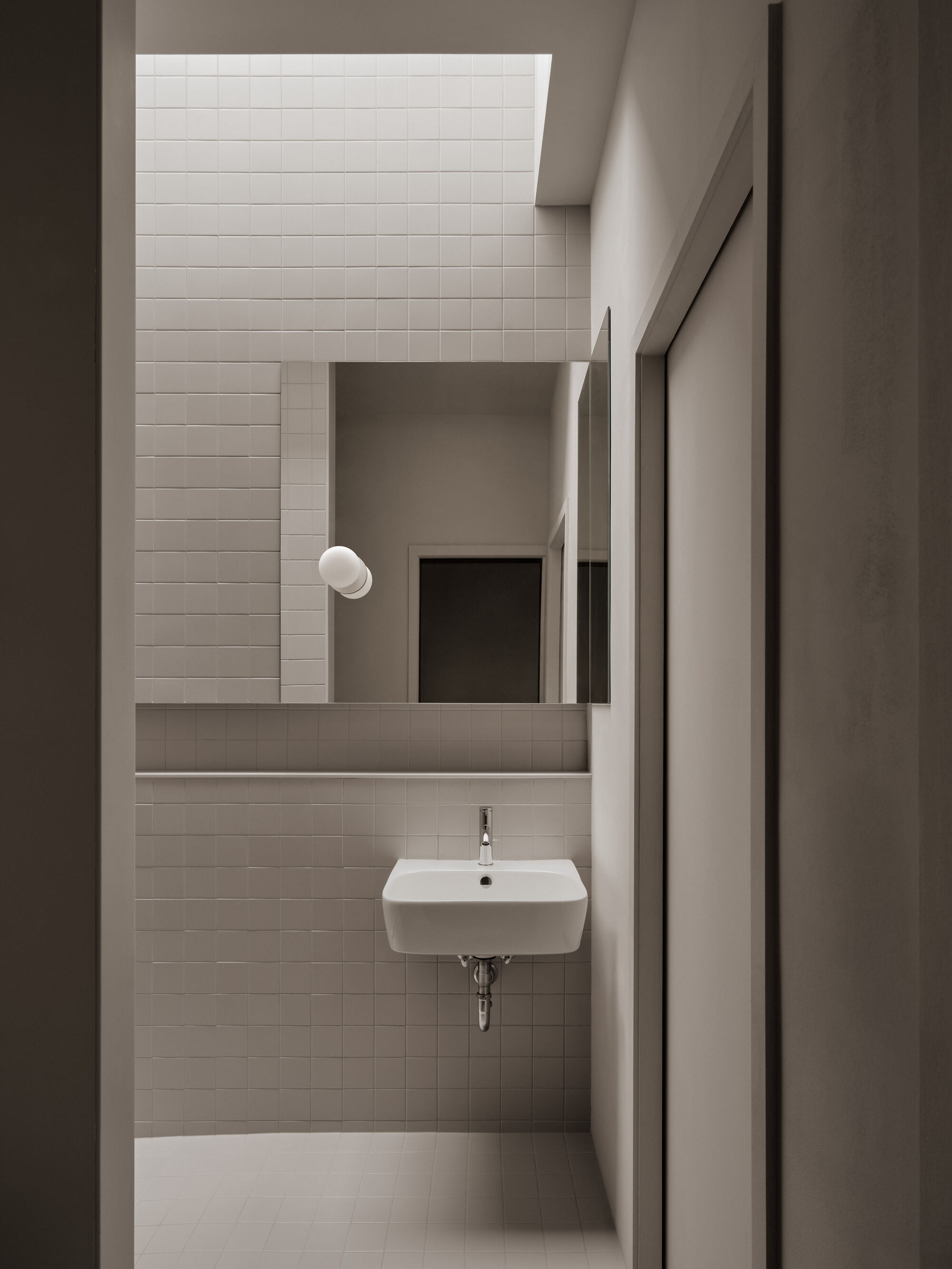 Narrow bathroom with white rectangular tile walls and a wall-mounted sink beneath a skylight