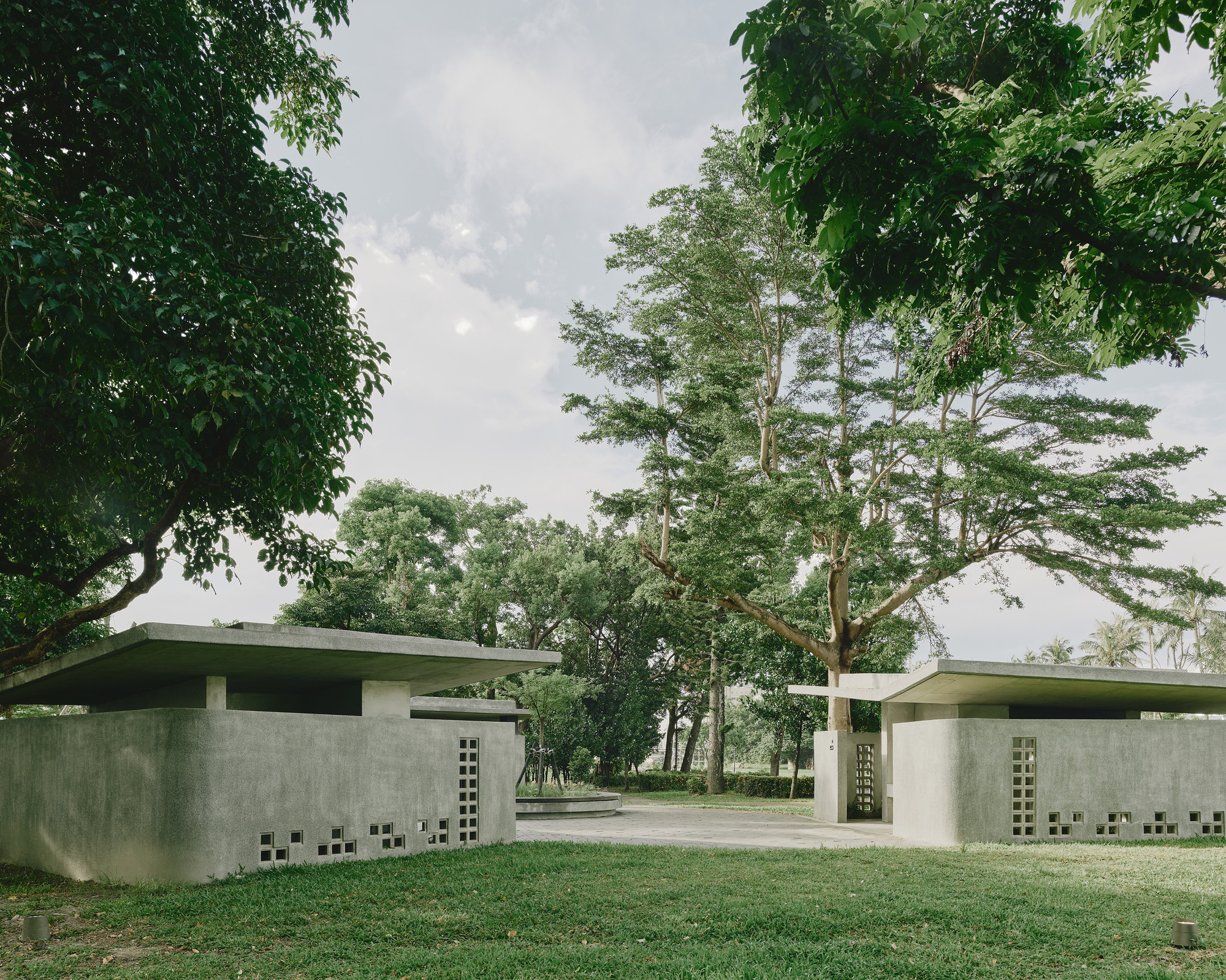 Entry path between two low concrete structures with cantilevered roofs and patterned openings