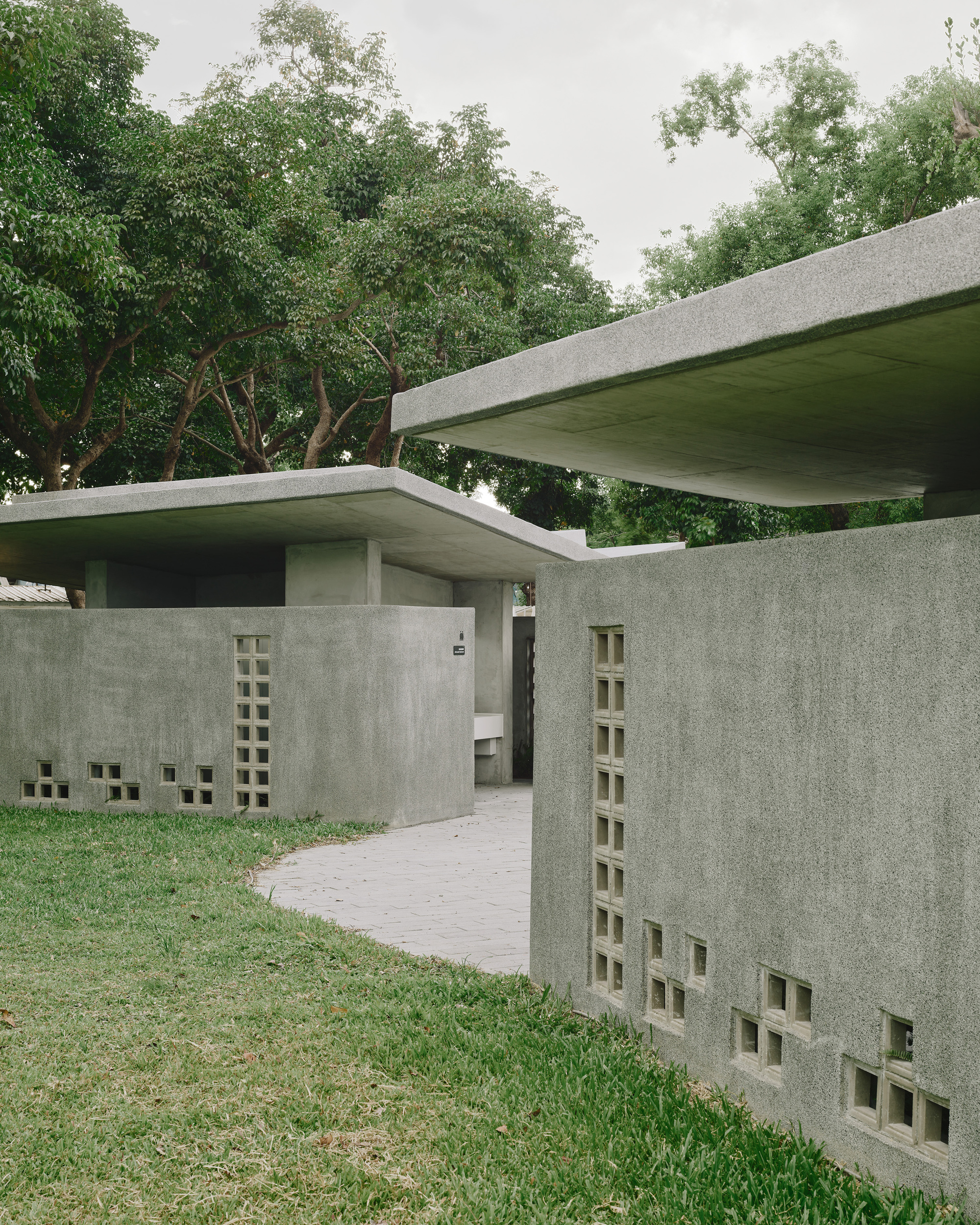 Curved brick pathway leading between concrete walls with staggered square openings and overhanging roofs