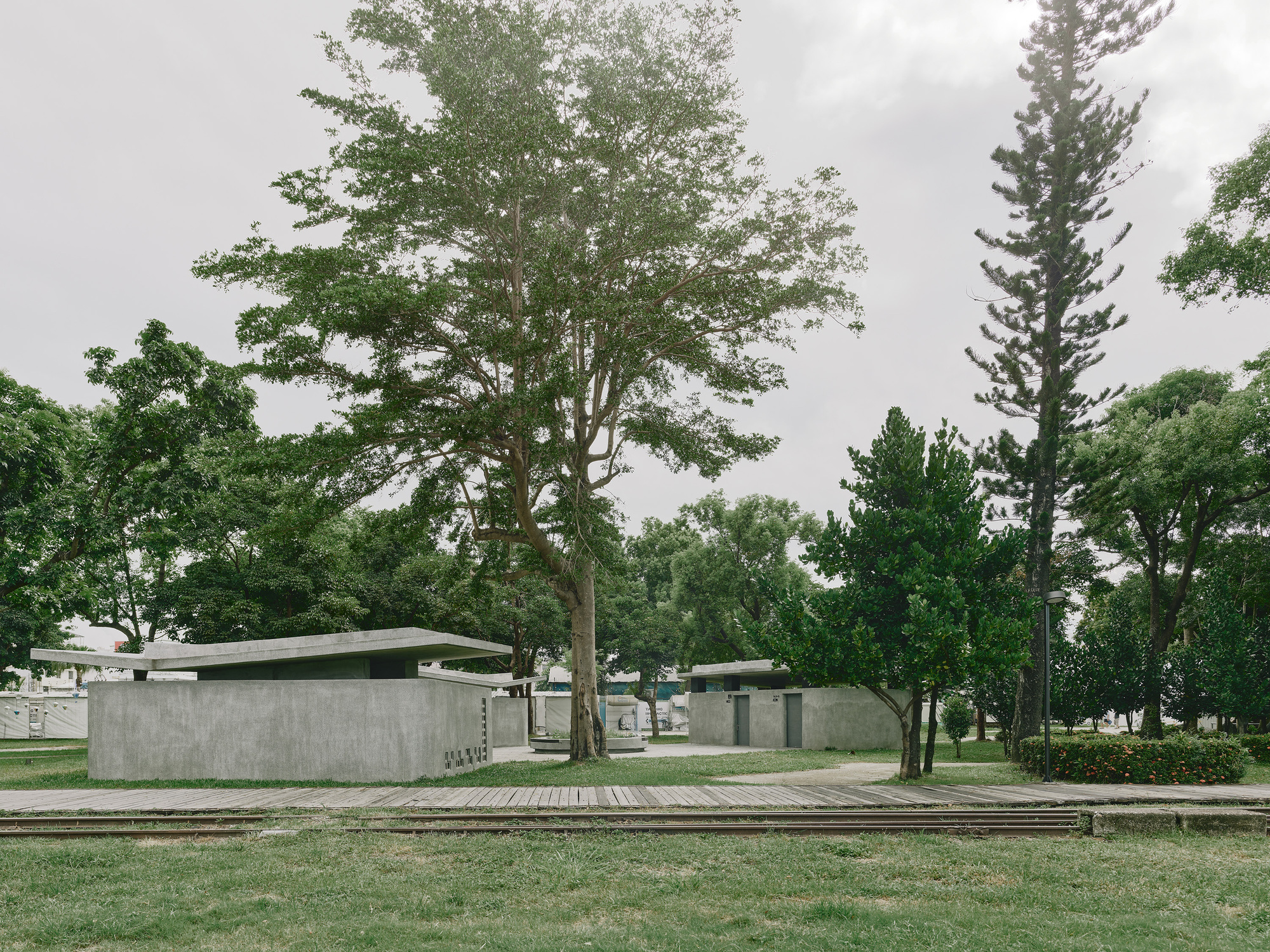 Low pavilion structures with board-formed concrete walls and thin roof planes among scattered trees