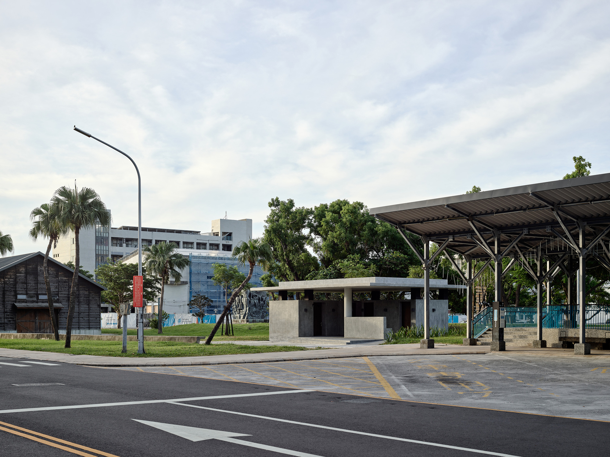 Street view of the concrete pavilion with adjacent steel and timber canopy structure at dusk
