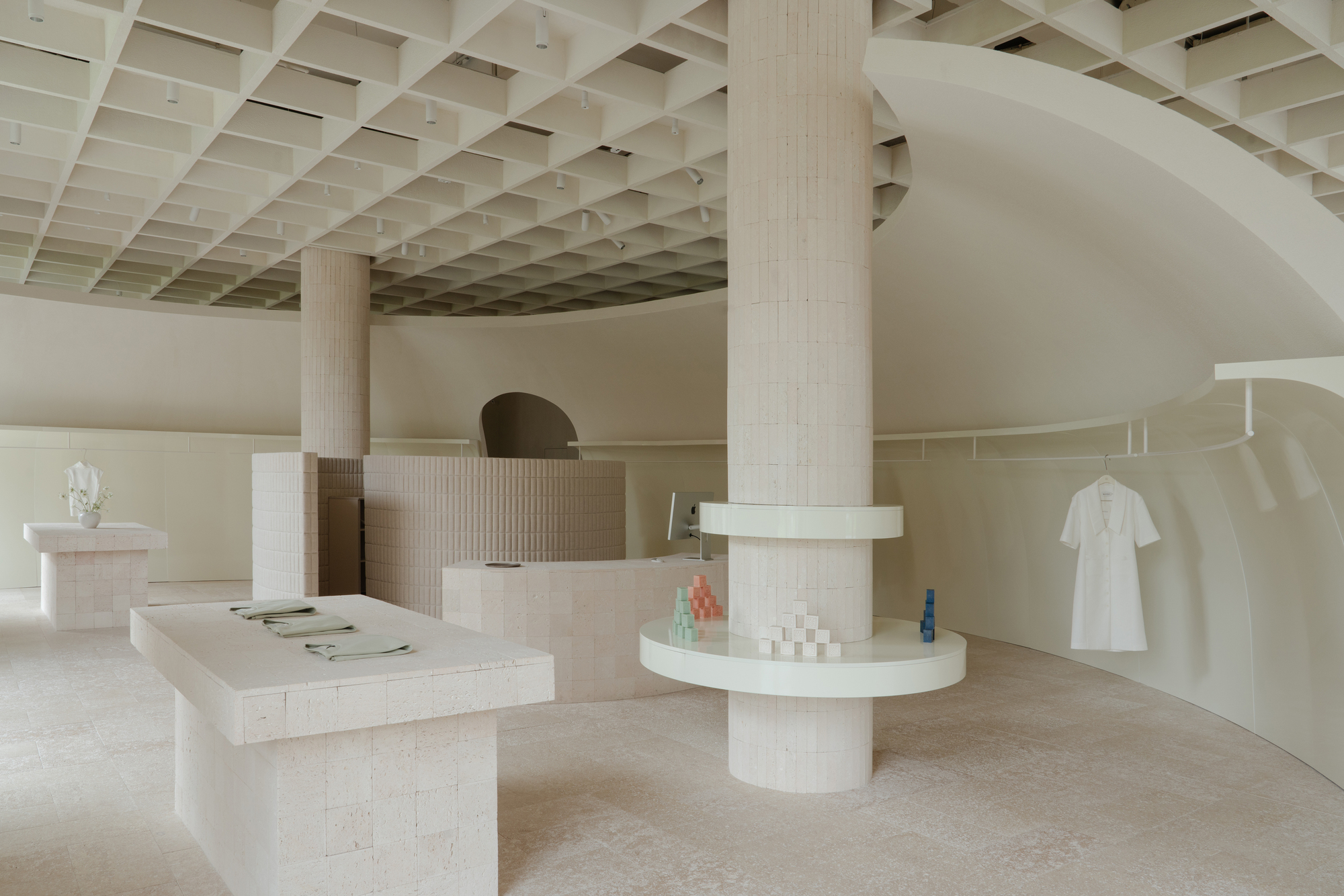 Interior retail space with coffered timber ceiling, fluted columns, and curved display walls in pale plaster