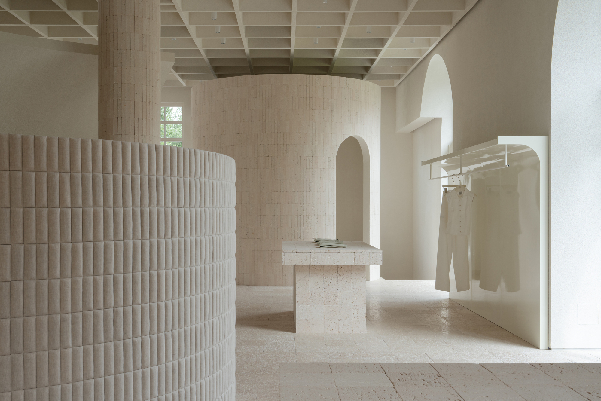 View through arched openings showing fluted cylindrical volume and stone display plinths under gridded ceiling