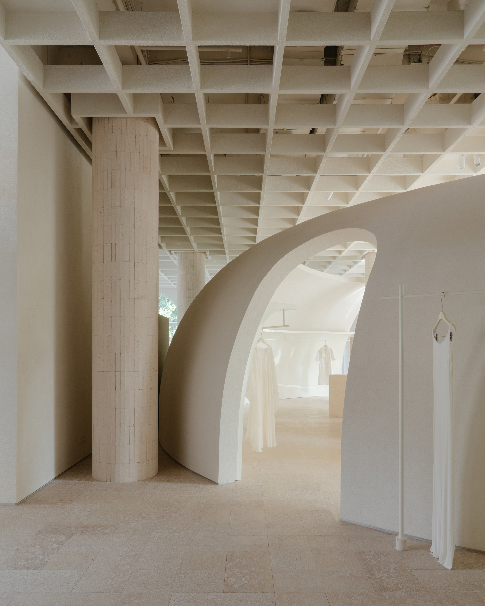 Curved archway framing fluted column and recessed display niches with hanging garments in daylight