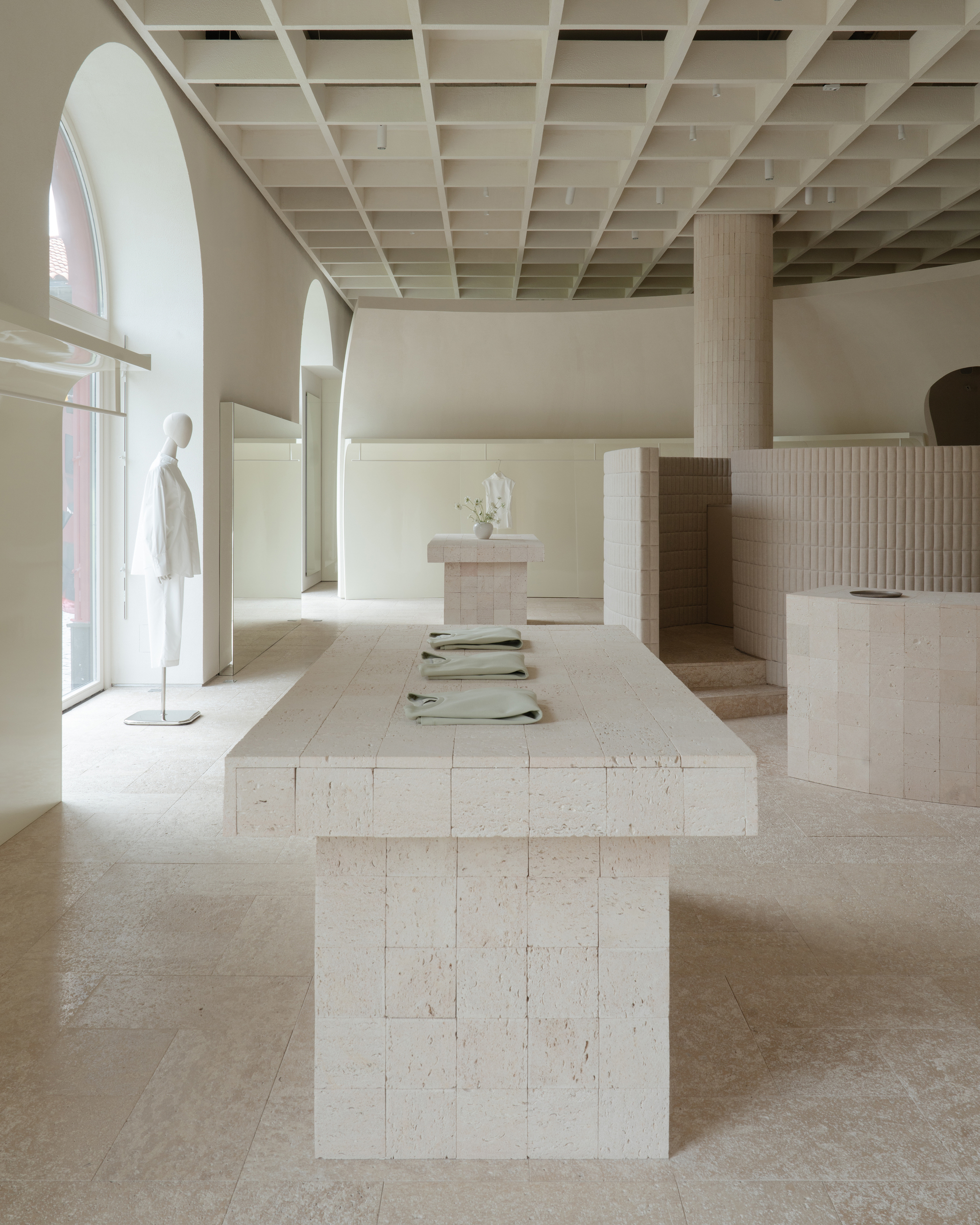 Long stone display table with arched windows and mannequin under exposed timber coffered ceiling