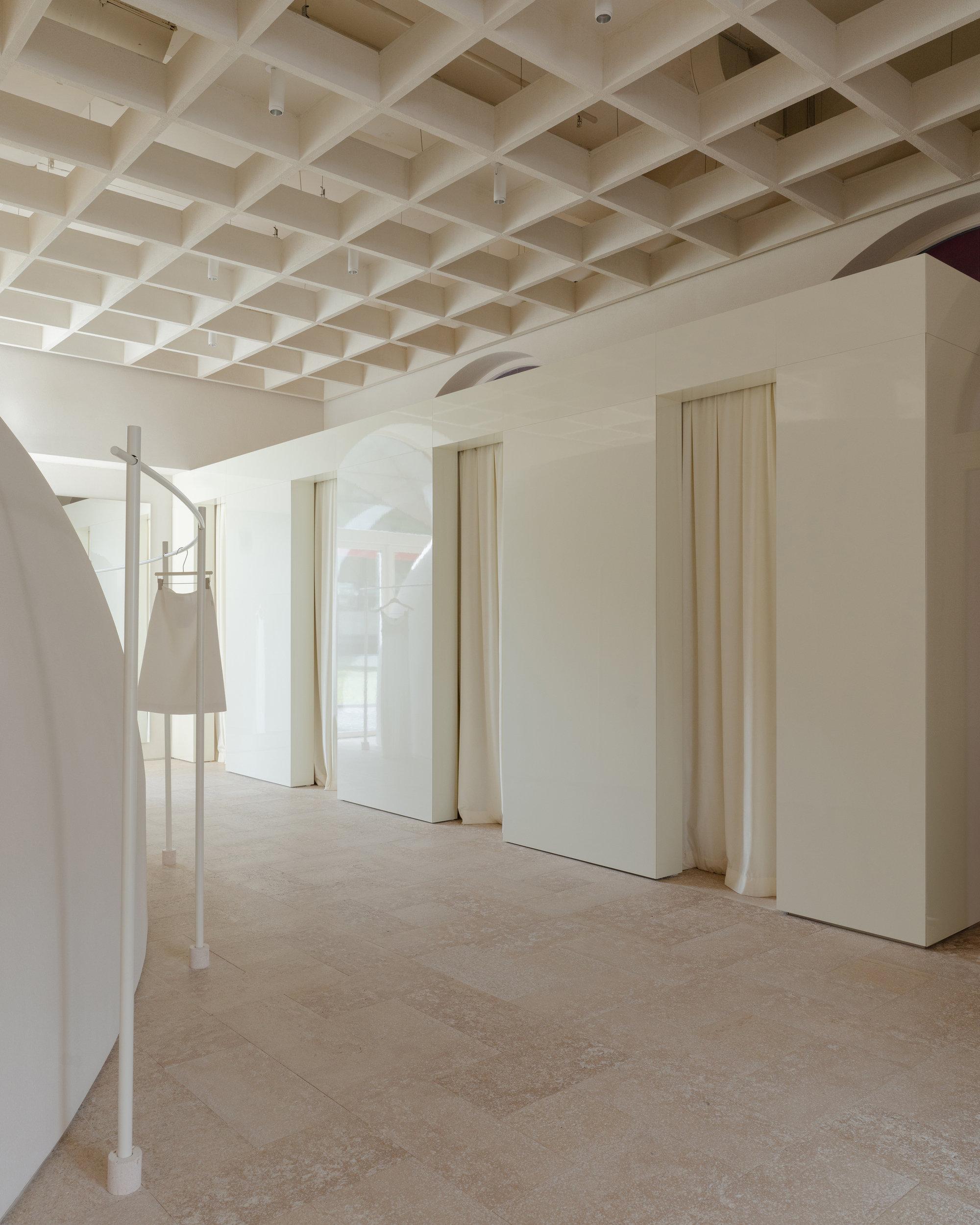 Interior corridor with coffered ceiling grid and pale vertical-plank doors set in curved white walls