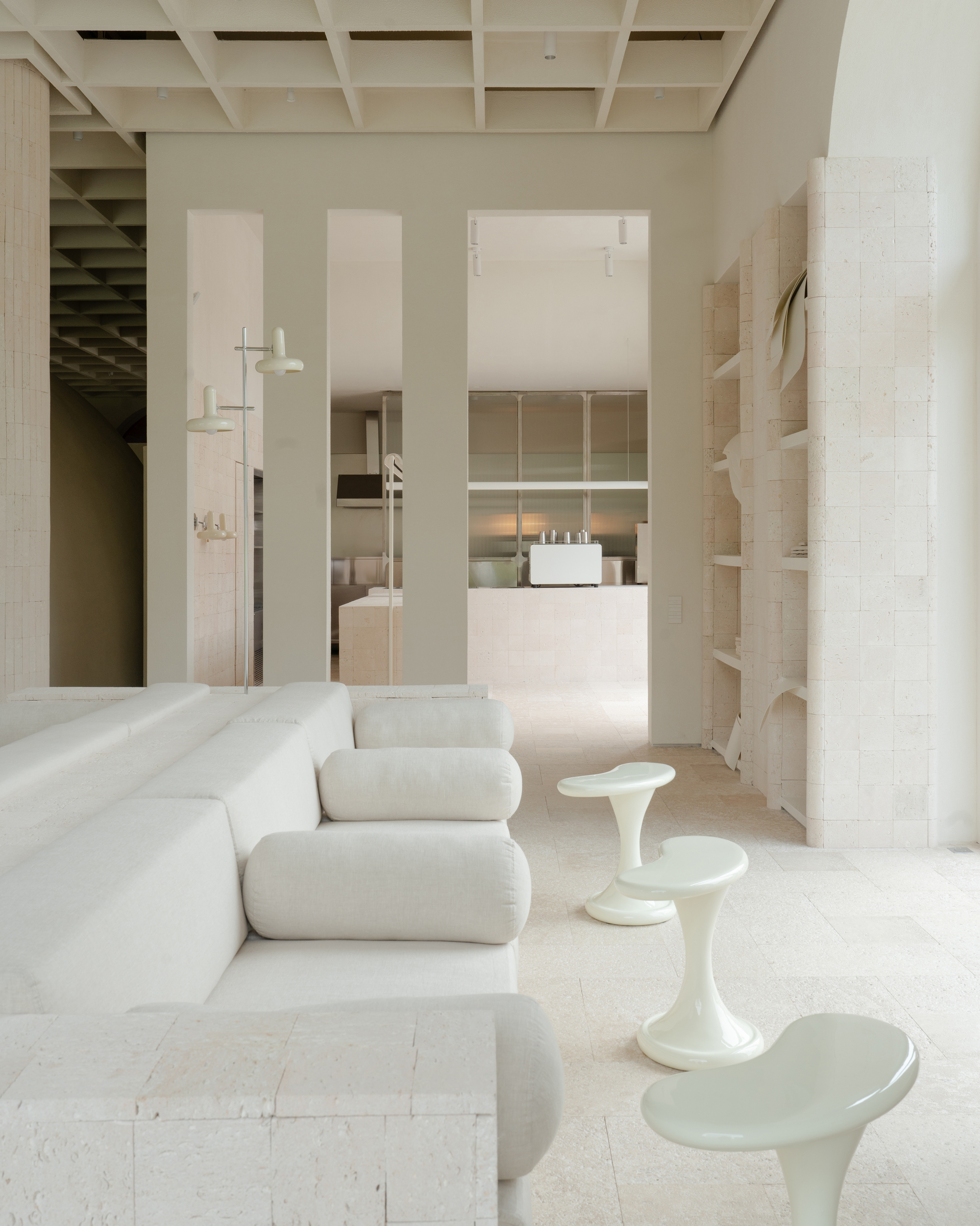 Open plan living space with pale upholstered seating and sculptural side tables under gridded ceiling