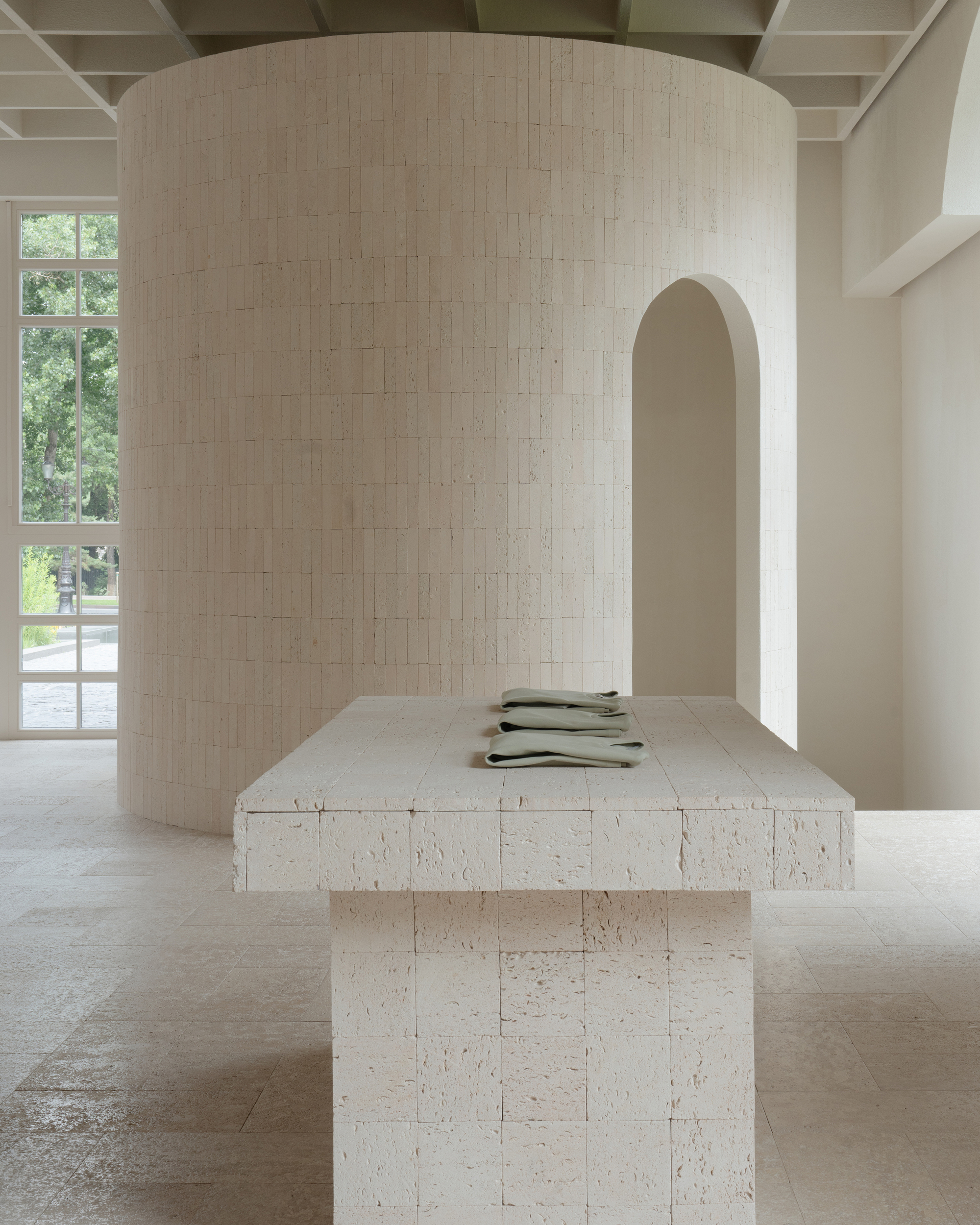 Textured limestone block table beside a curved cylindrical wall with an arched doorway in soft daylight