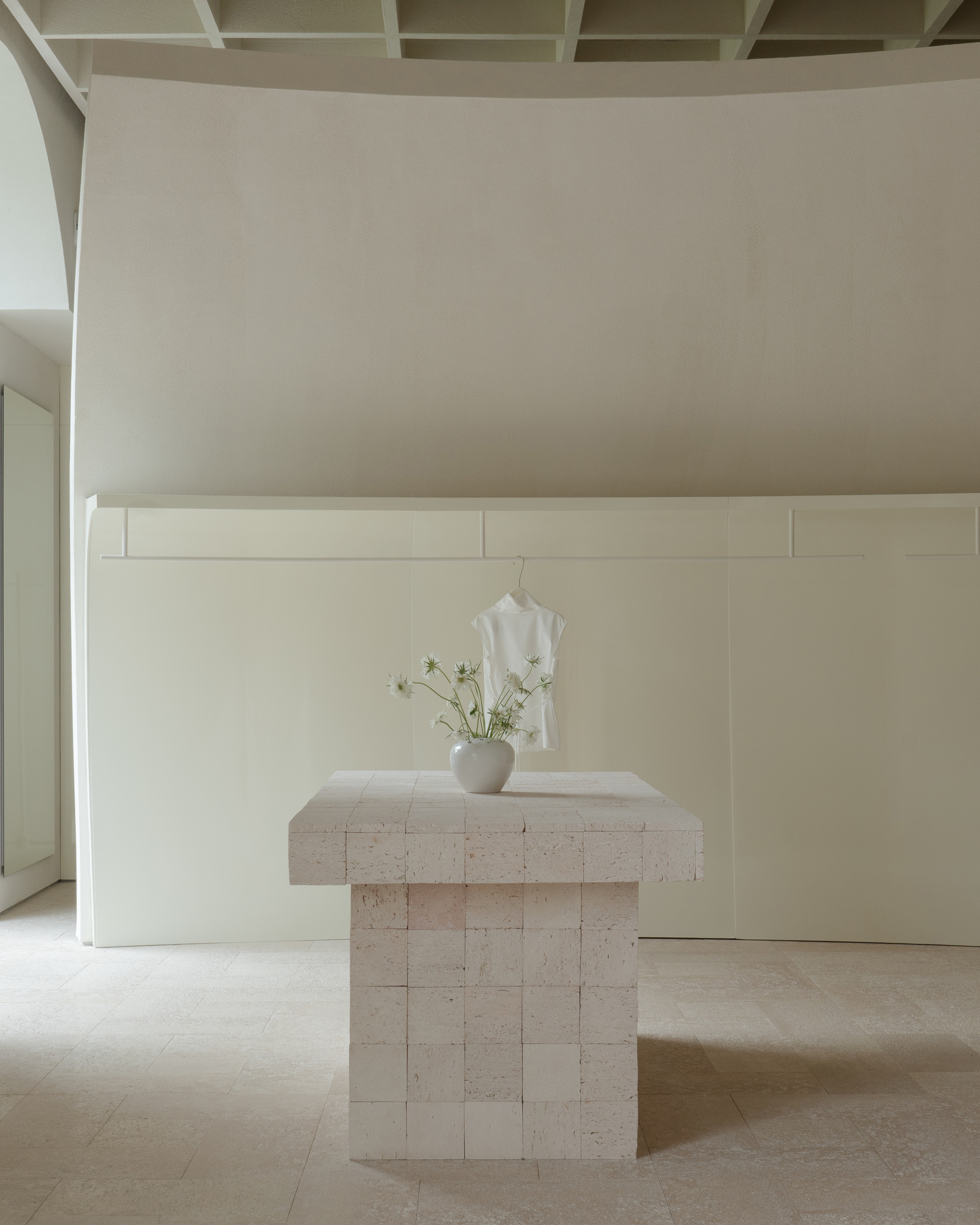Travertine pedestal table with a vase of white flowers beneath a coffered ceiling and paneled wall