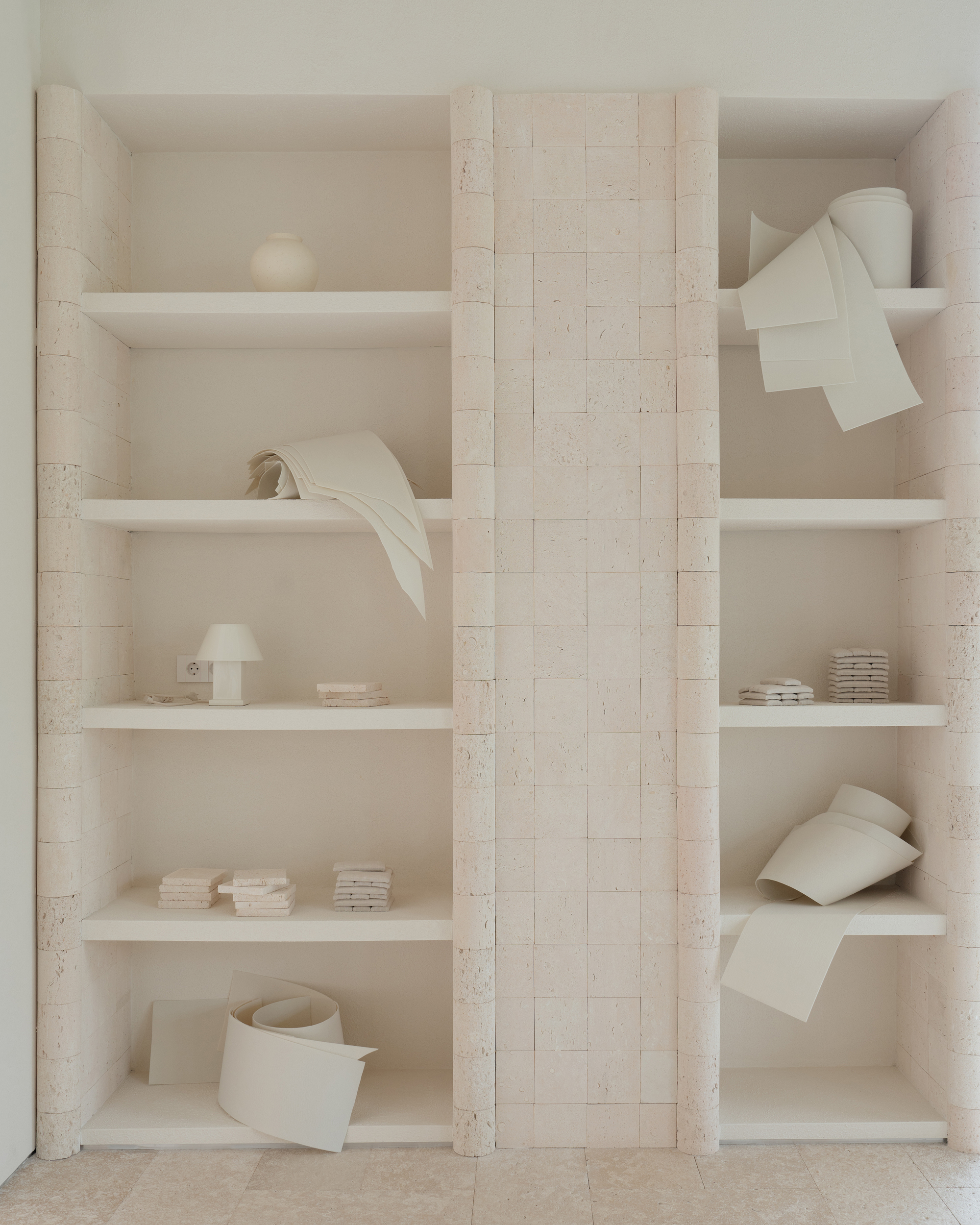 Floor-to-ceiling shelving unit with cream-colored books and paper sculptures flanking a limestone block column
