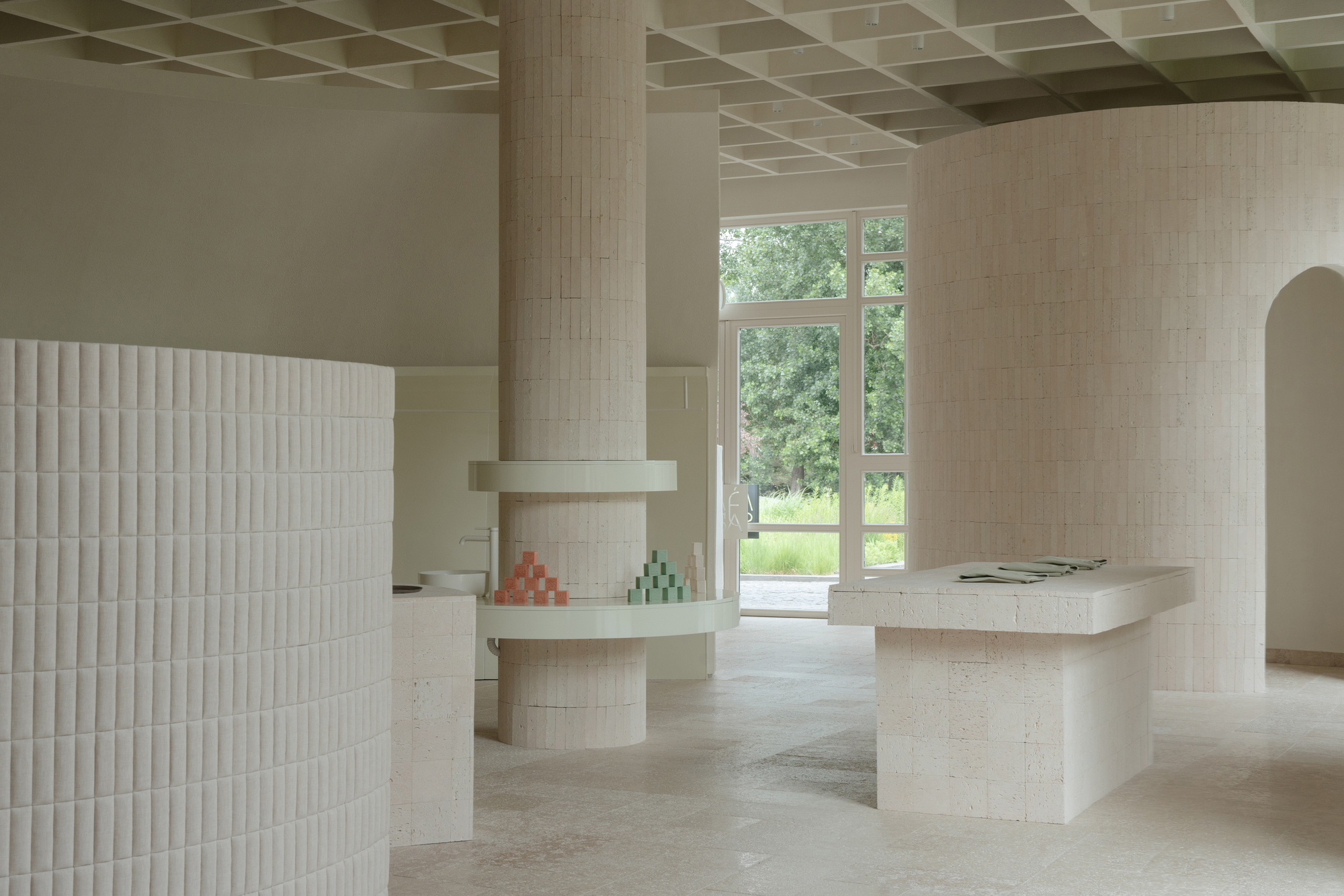 Interior with pale brick columns and coffered ceiling framing a view to the garden beyond