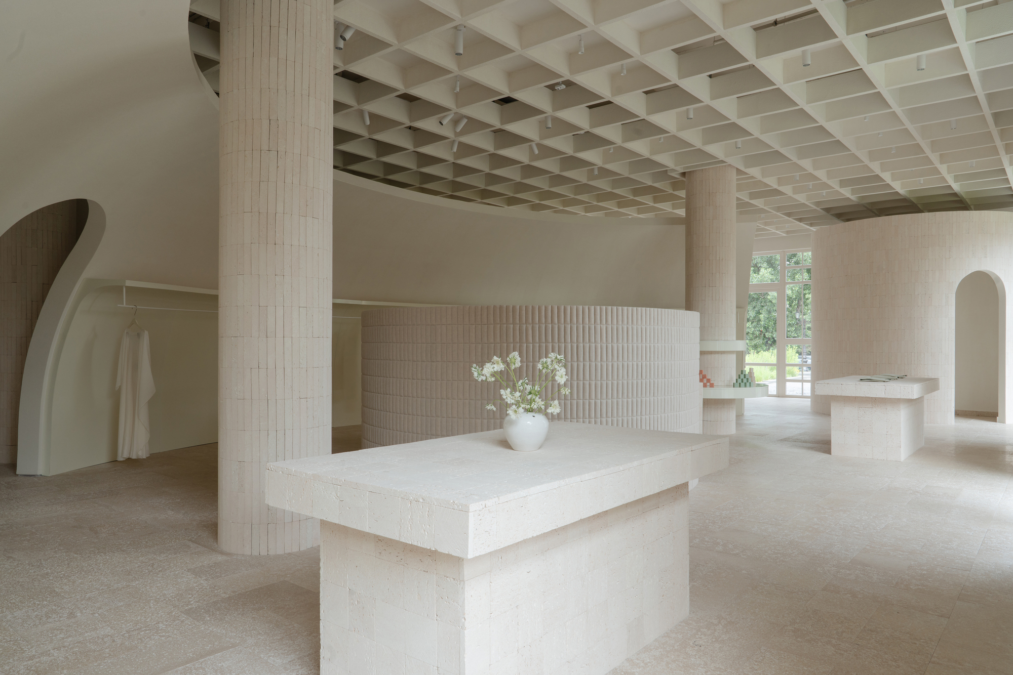 Textured brick island with white vase of flowers beneath a gridded timber ceiling