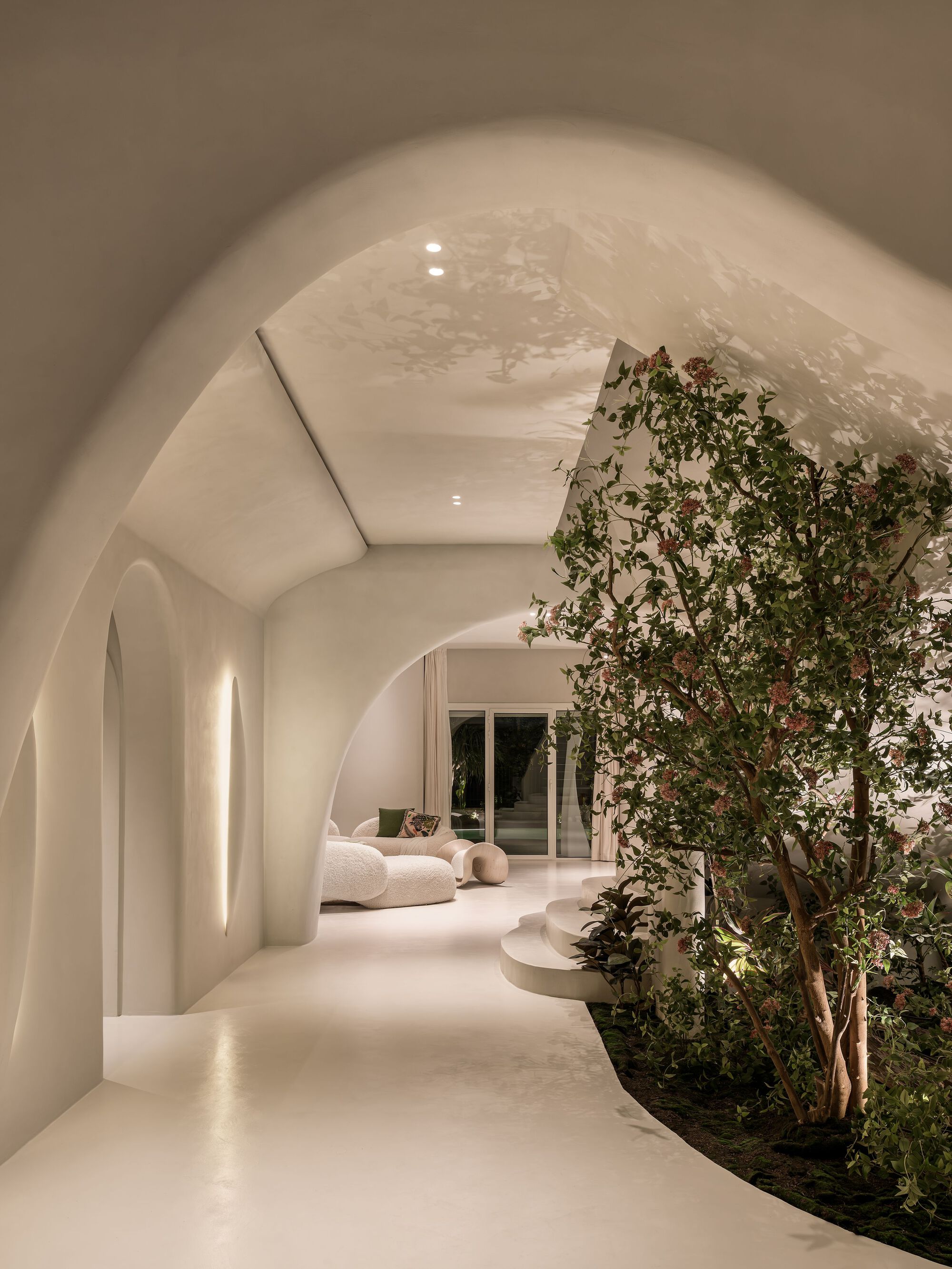 Vaulted corridor with planted trees along one side and warm artificial lighting at night