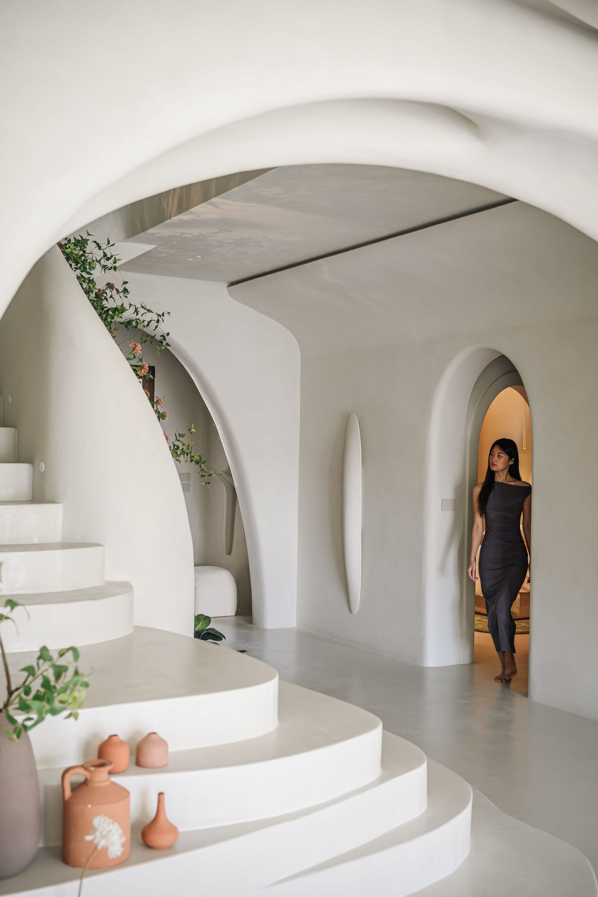 White curved staircase with integrated planters and arched doorway where a woman stands in afternoon light