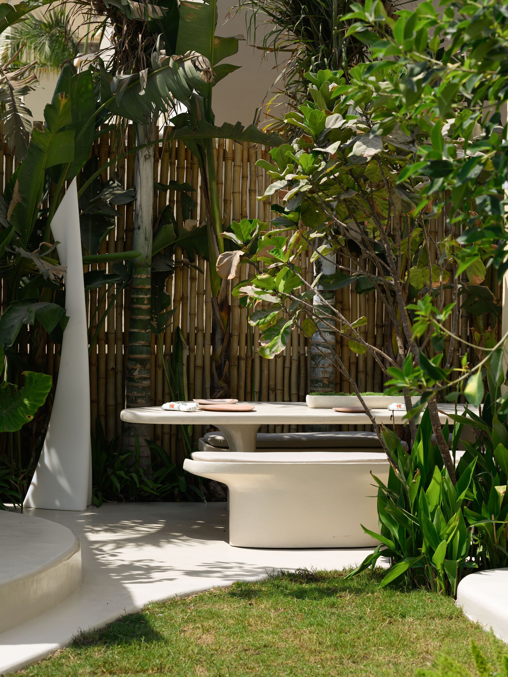Courtyard seating area with bamboo screen wall and dense tropical planting in dappled sunlight
