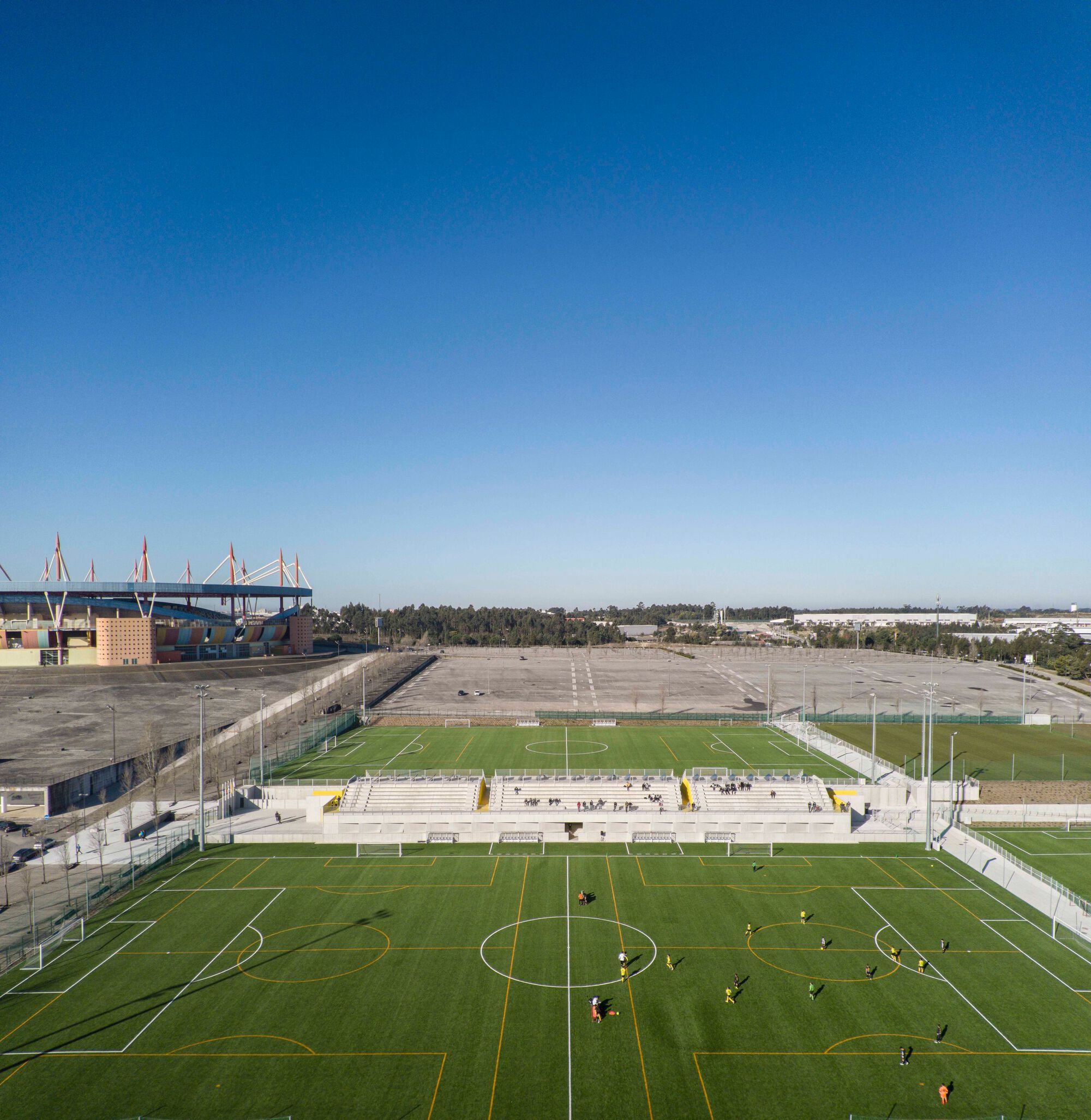 Elevated view of multiple football pitches with players training under a clear blue sky