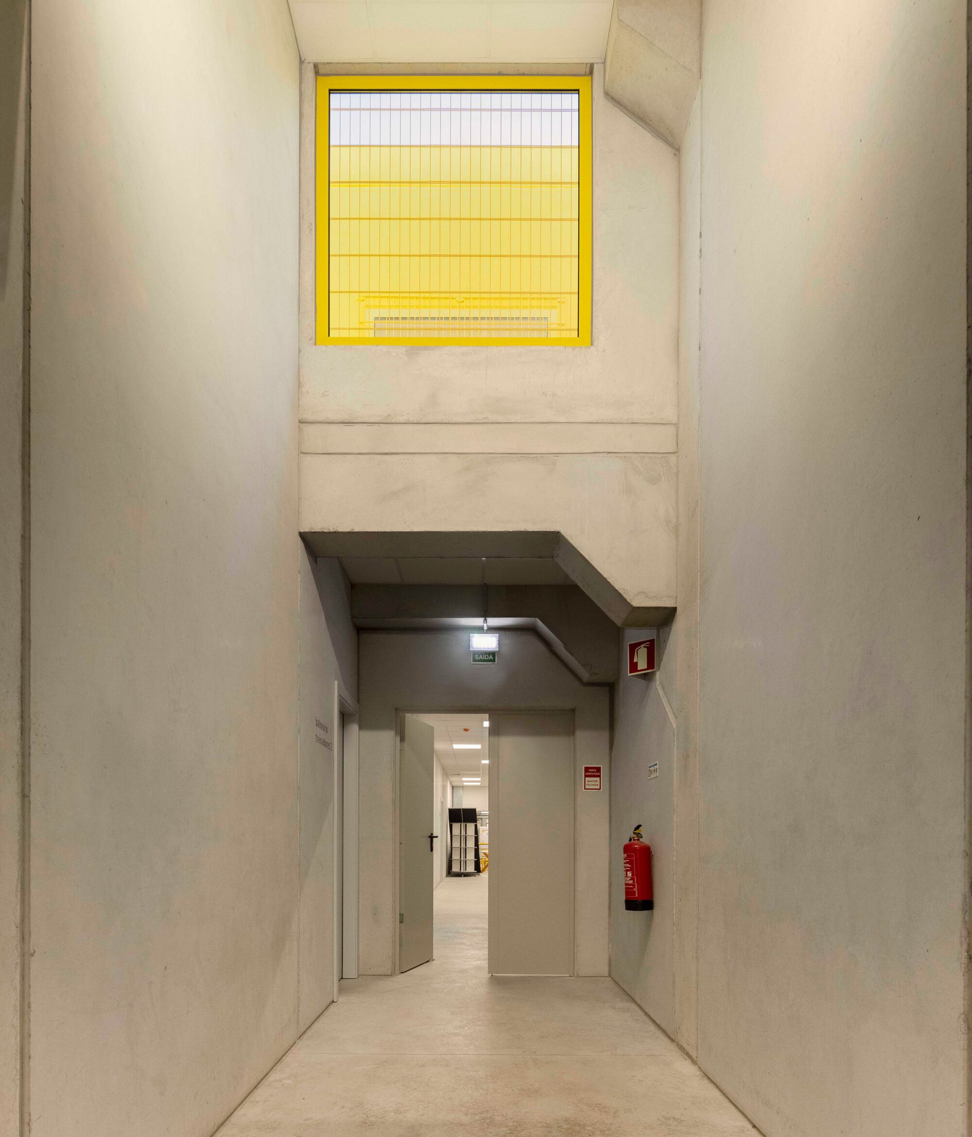 Double-height interior passage with yellow wire glass window above doorway in cast concrete walls