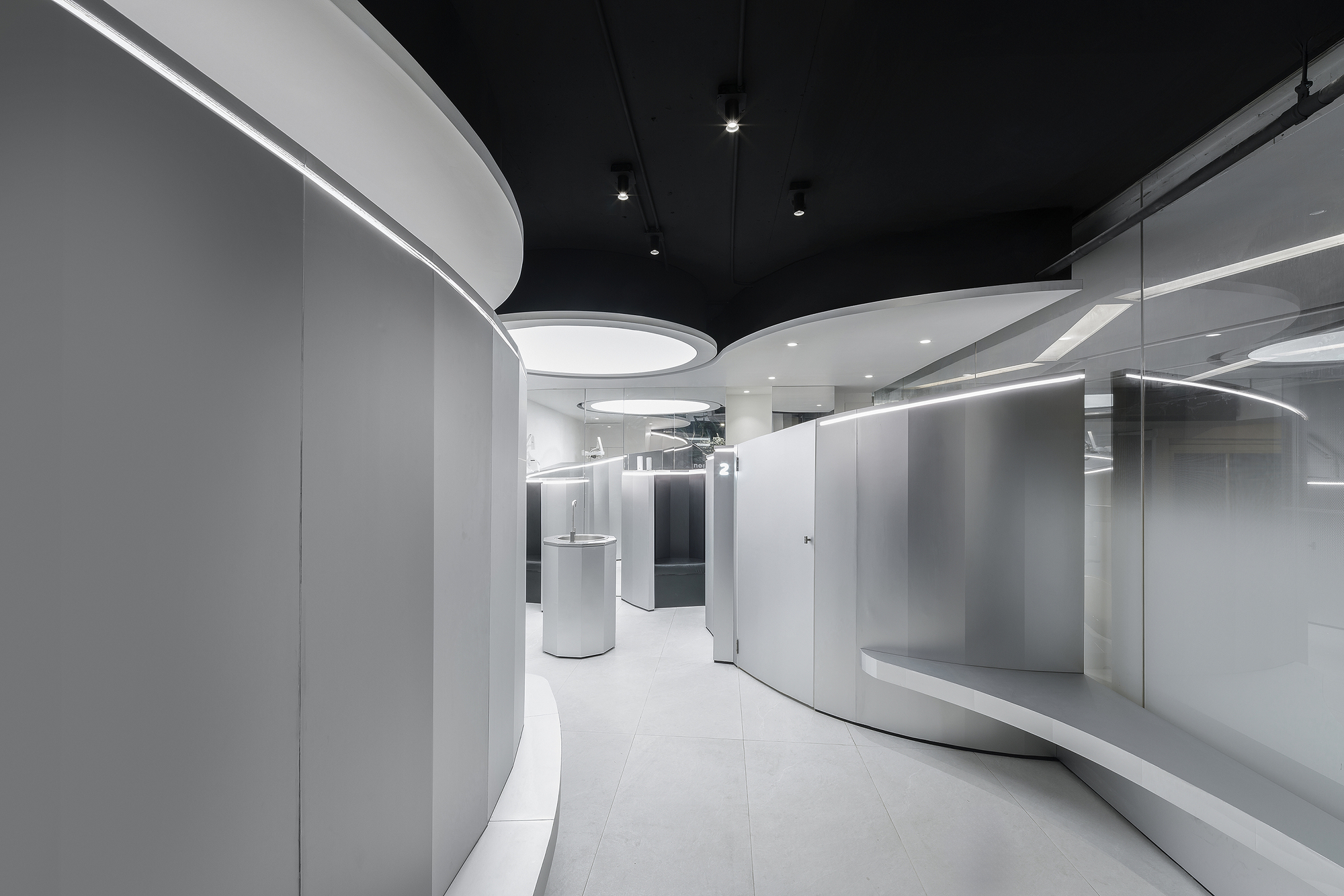 Curved white walls with integrated linear lighting beneath a black ceiling with circular recessed fixtures