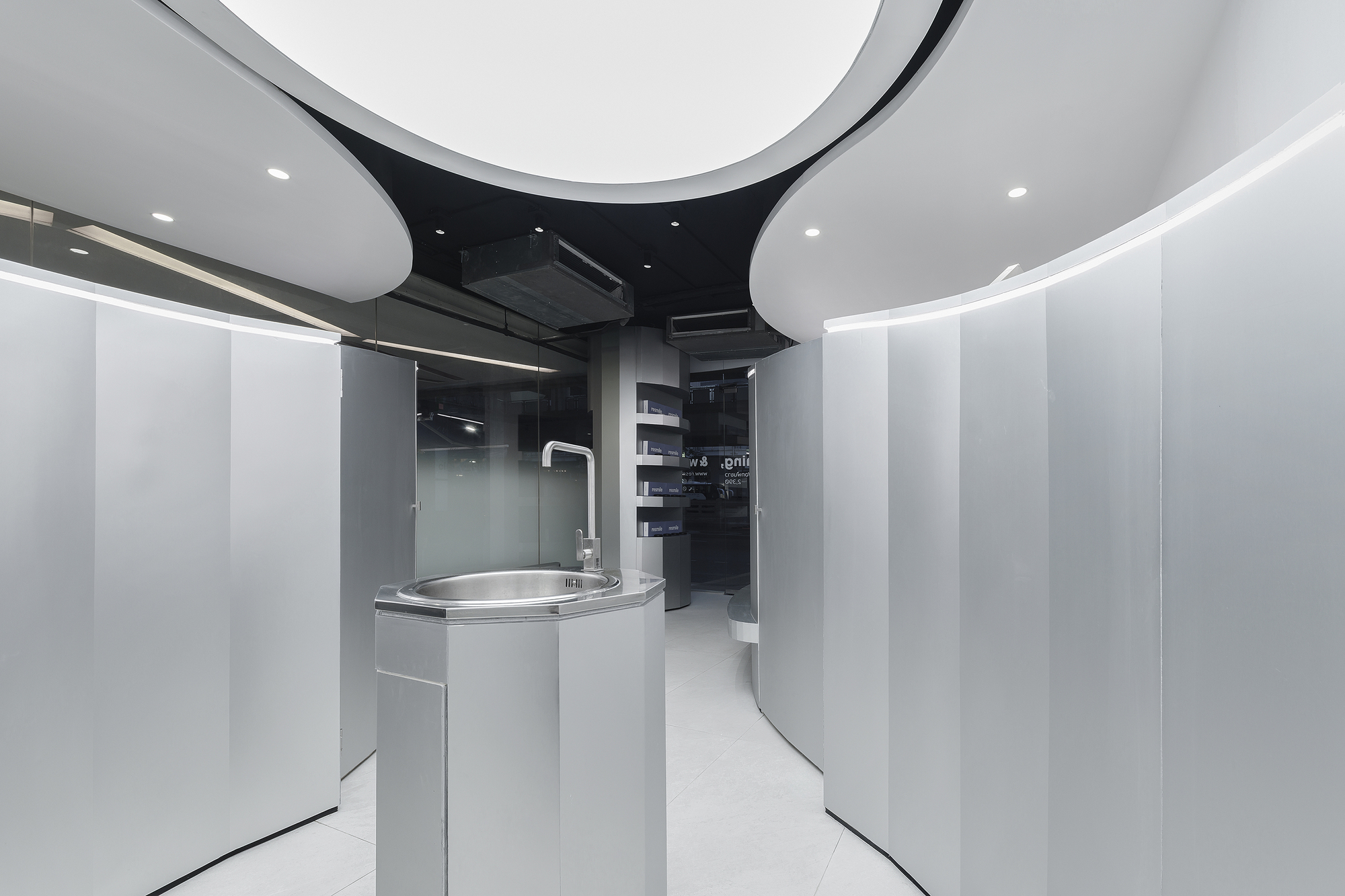Curved white corridor with cylindrical handwashing unit and black ceiling revealing exposed mechanical systems