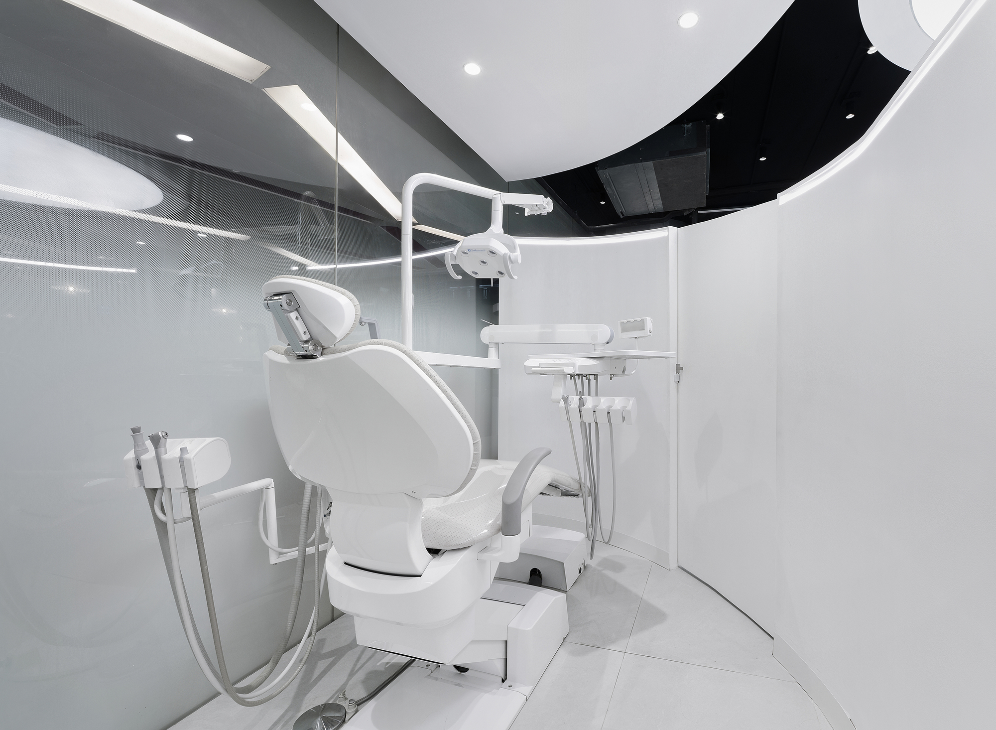 Dental chair with overhead lamp and equipment arm in a glazed treatment room with curved ceiling