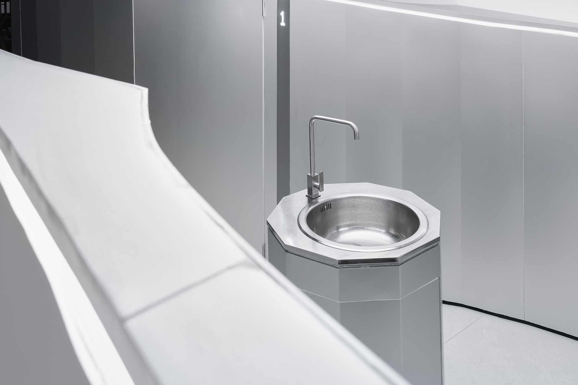 Detail of octagonal sink basin with metal bowl and tap against grey wall panels