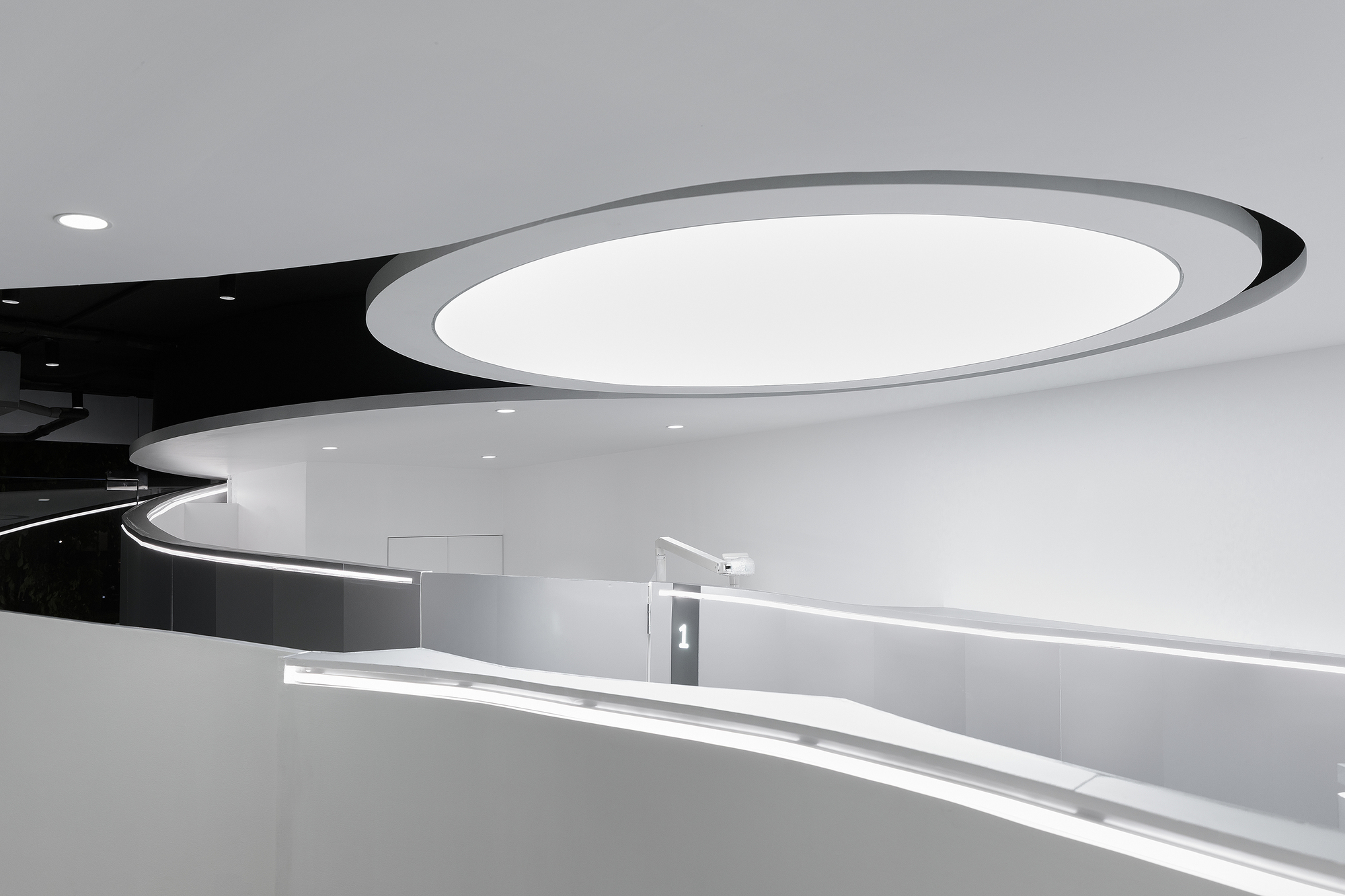 Curved reception counter with integrated LED strip lighting beneath an oval ceiling coffer with black accent