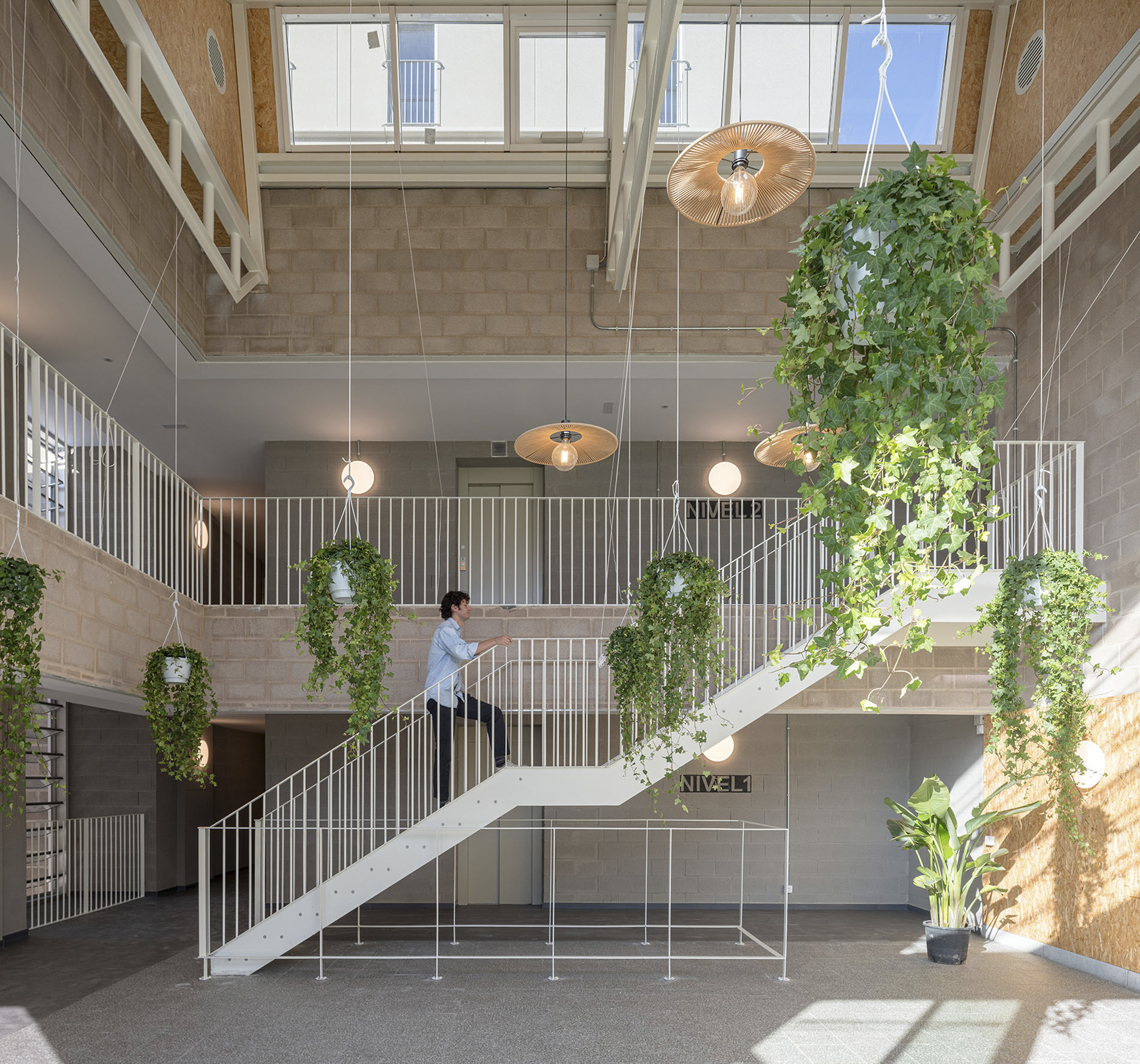Double-height atrium with suspended planters and a white steel staircase beneath pendant lights