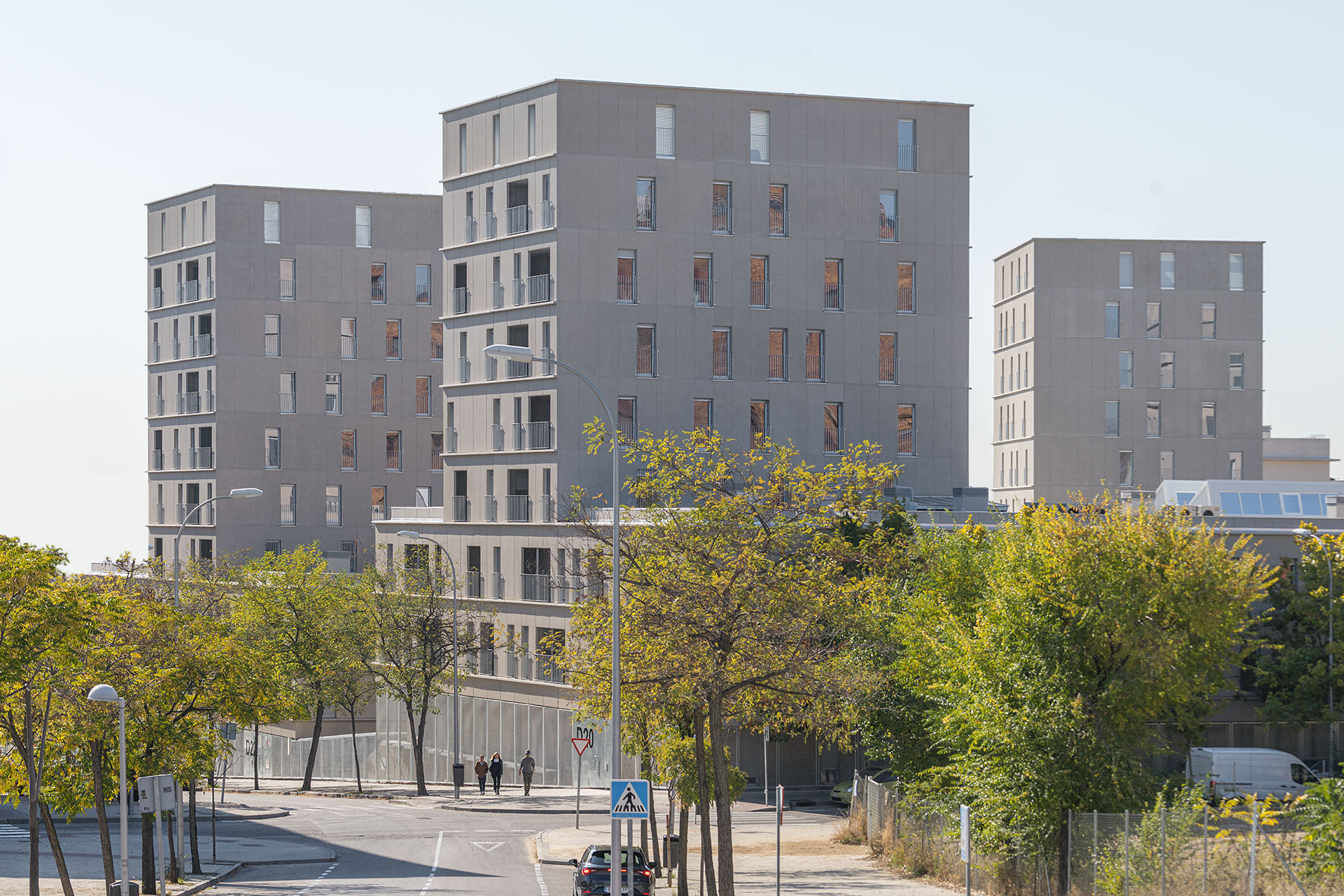 Three offset residential blocks with prefabricated concrete facades behind street trees in autumn foliage