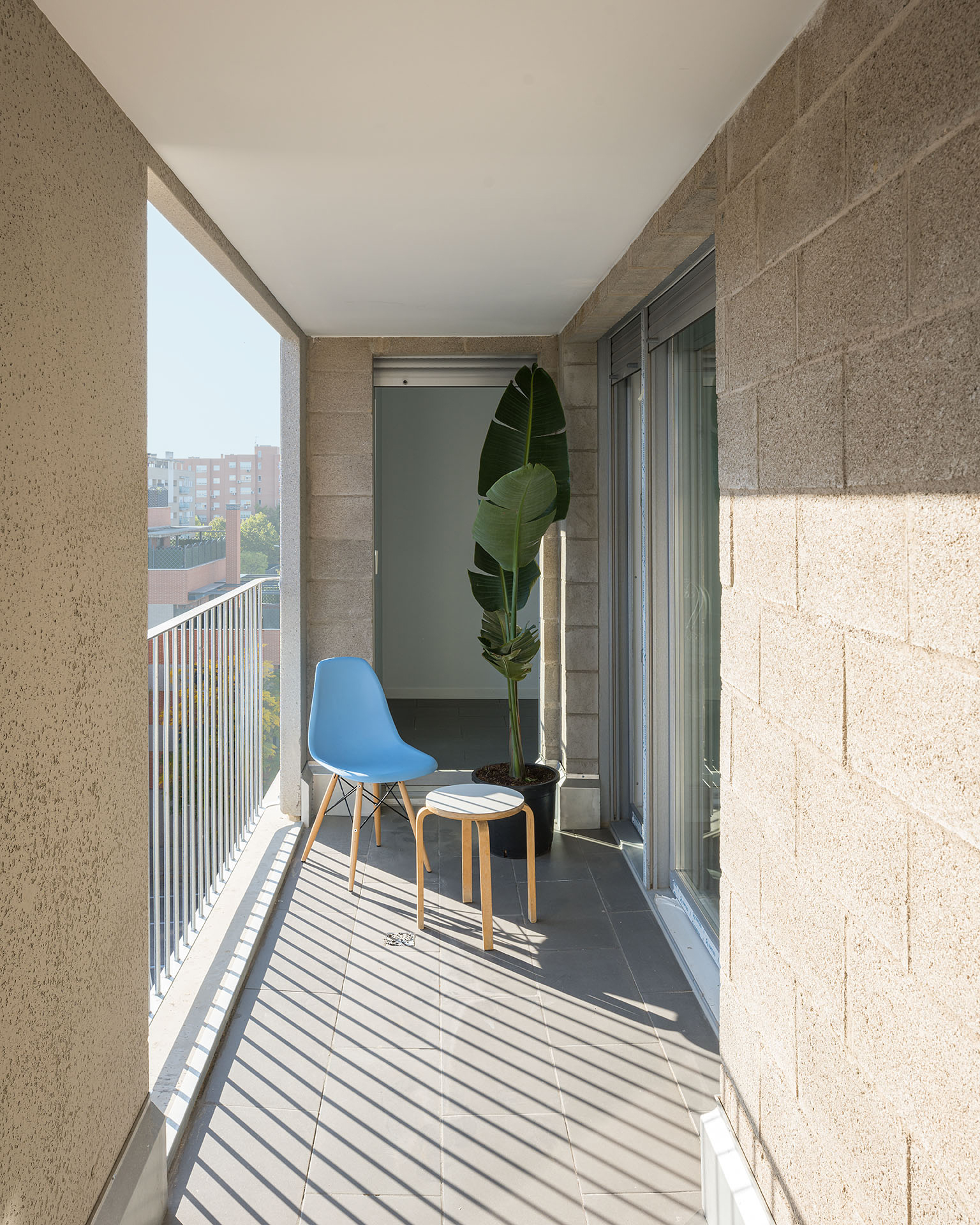 Narrow balcony with hempcrete block walls and vertical metal railings casting striped shadows