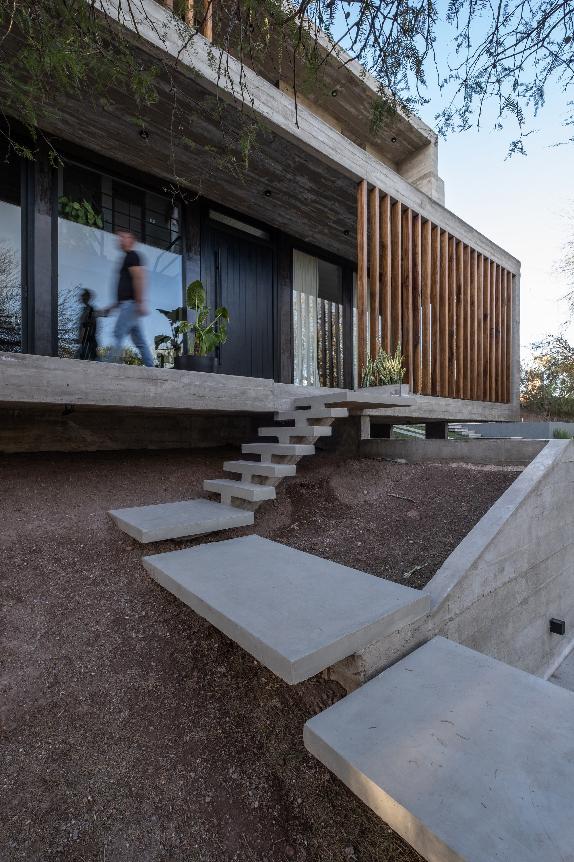 Floating concrete stair treads leading to upper terrace with timber brise-soleil and two figures in motion