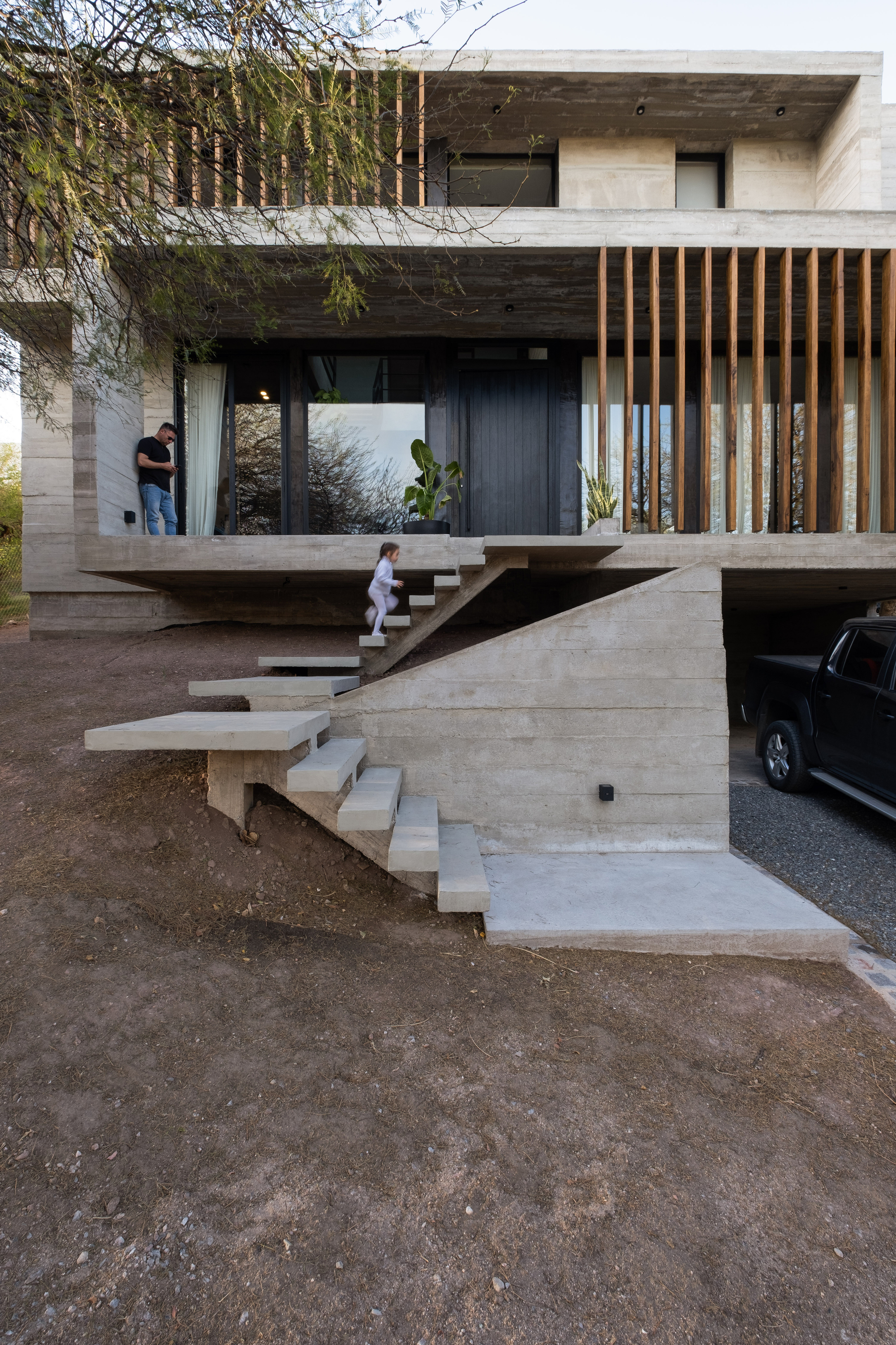 Branching cantilevered concrete stairs with two figures standing on upper terrace at dusk