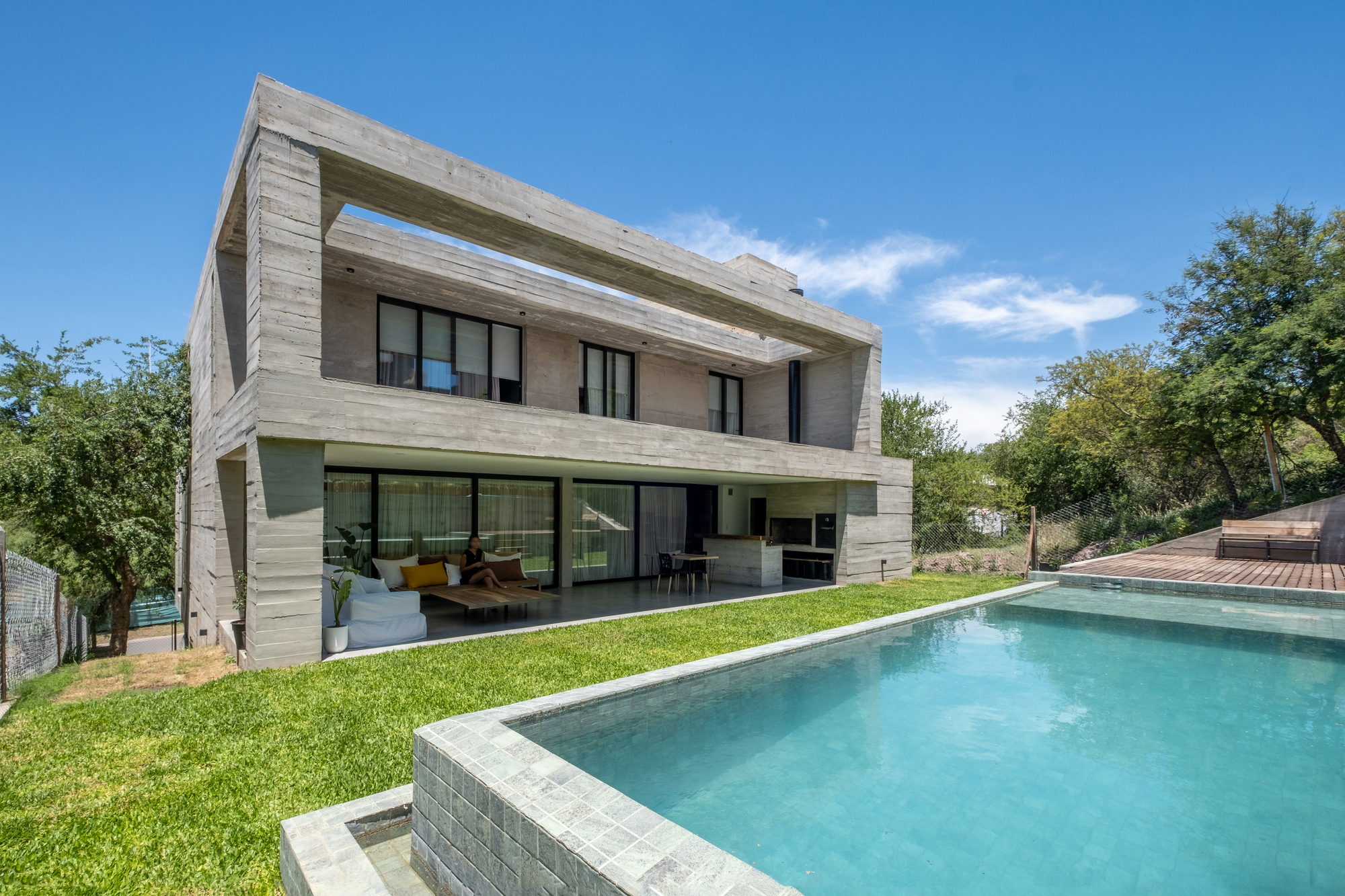 Board-formed concrete house with cantilevered upper floor overlooking a swimming pool and sloped lawn
