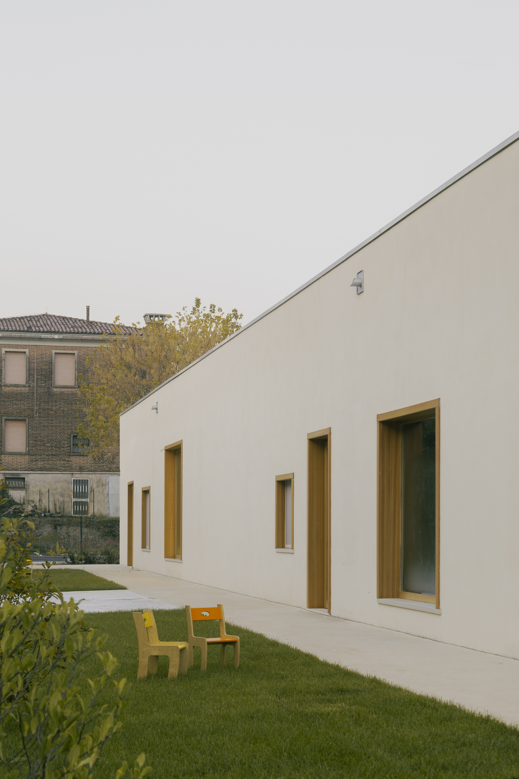 Angled stucco facade with timber-lined window reveals overlooking a courtyard with yellow furniture
