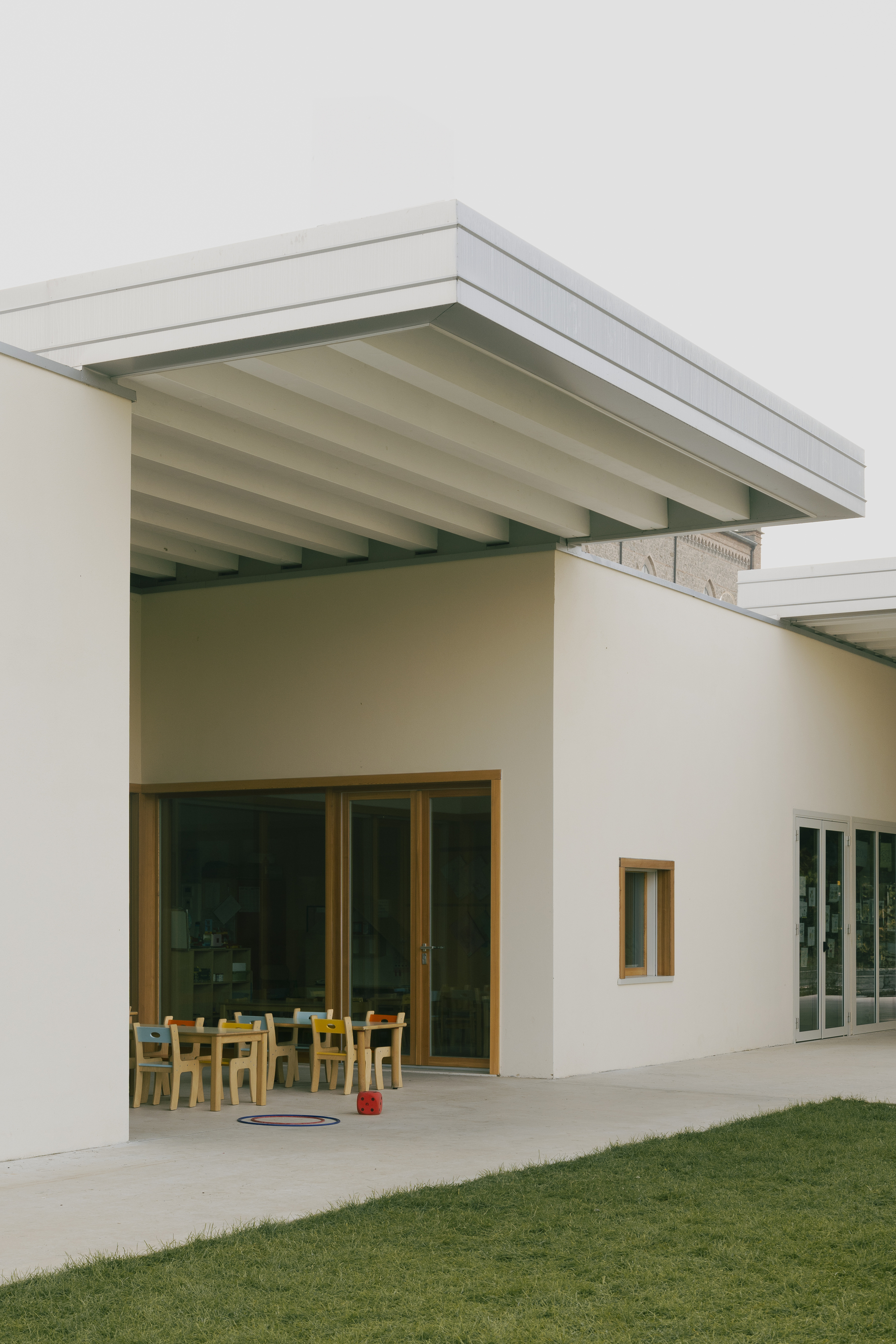 Covered outdoor terrace with exposed timber beams and wooden framed doors opening to a classroom space